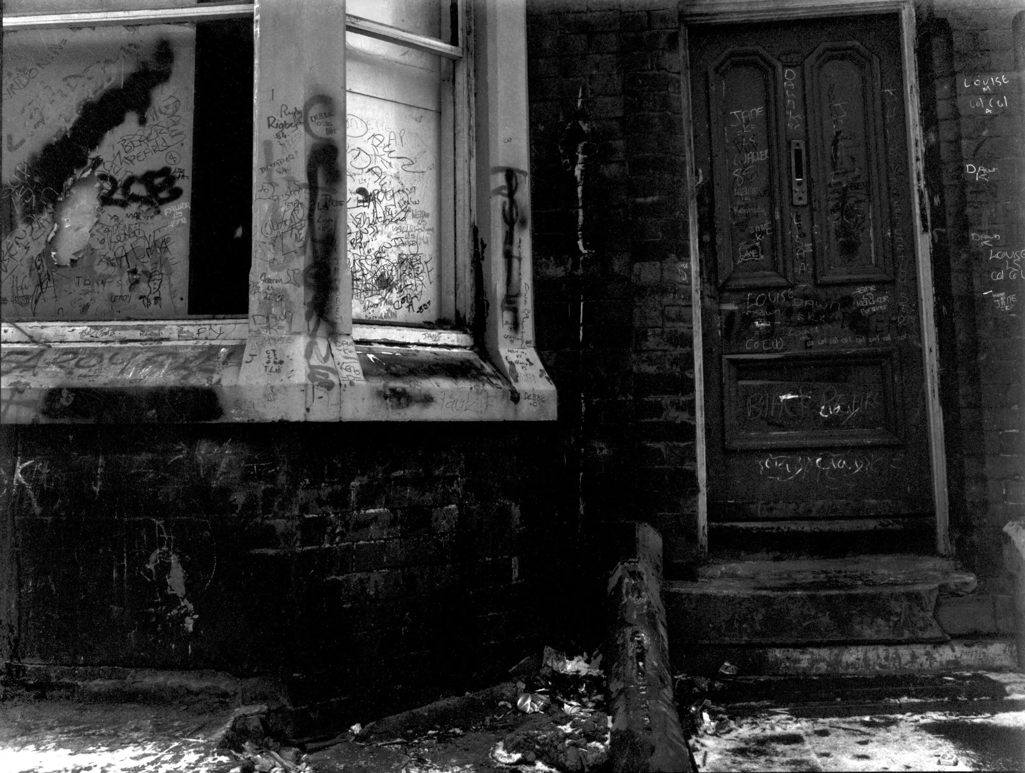 Black-and-white photo of a building's stairwell with graffiti-covered walls and a closed door, with the person's shadow cast on the wall.