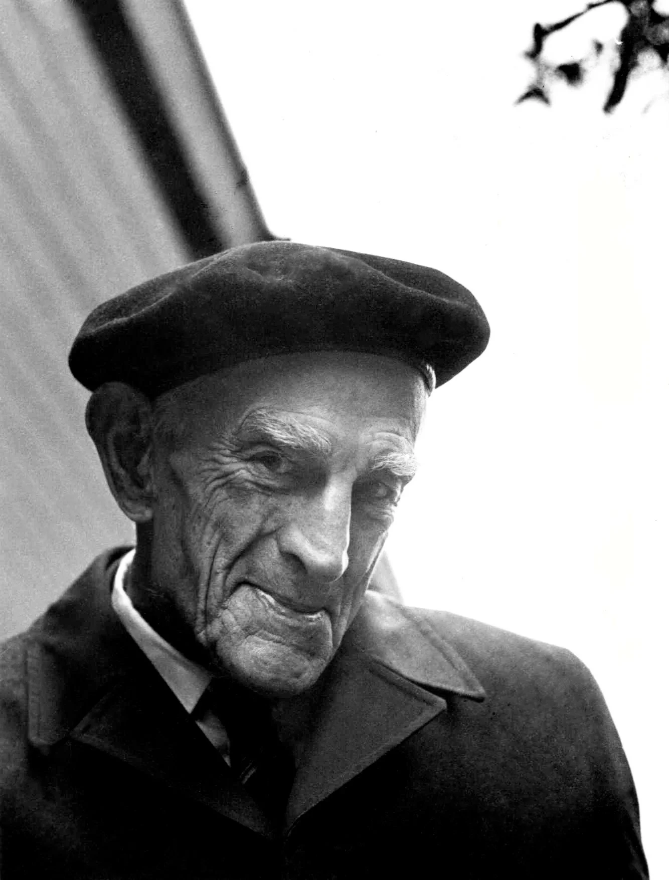 Close-up black-and-white photo of an elderly man with wrinkled face and a cap, with a somber expression.