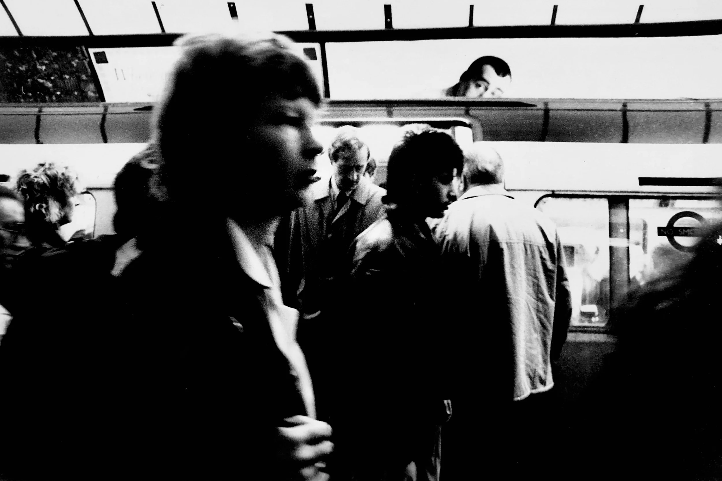Black and white photo of multiple people inside a subway train, some looking out the window or engaged in different activities.