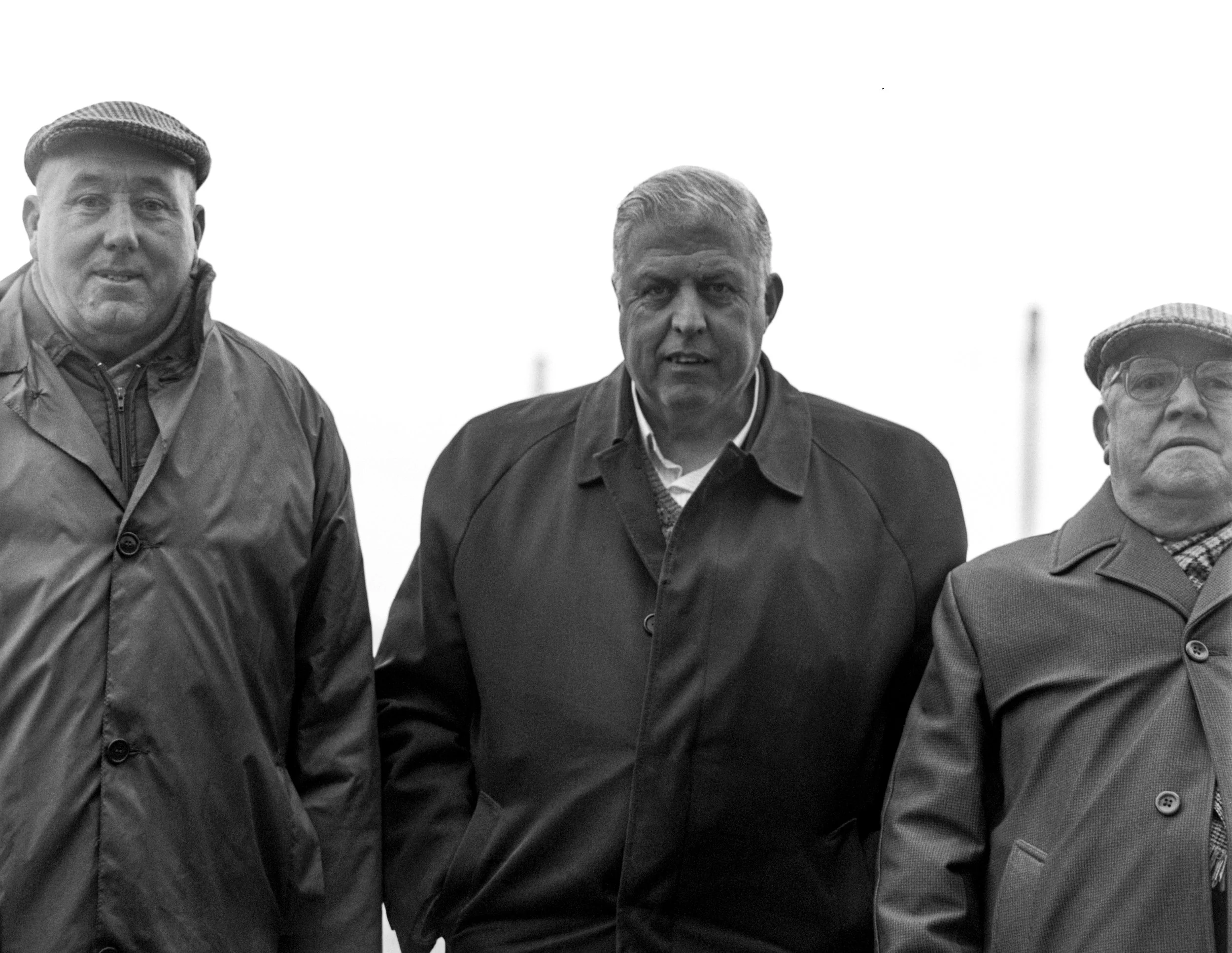 Black and white photo of three men standing outdoors wearing jackets and hats.