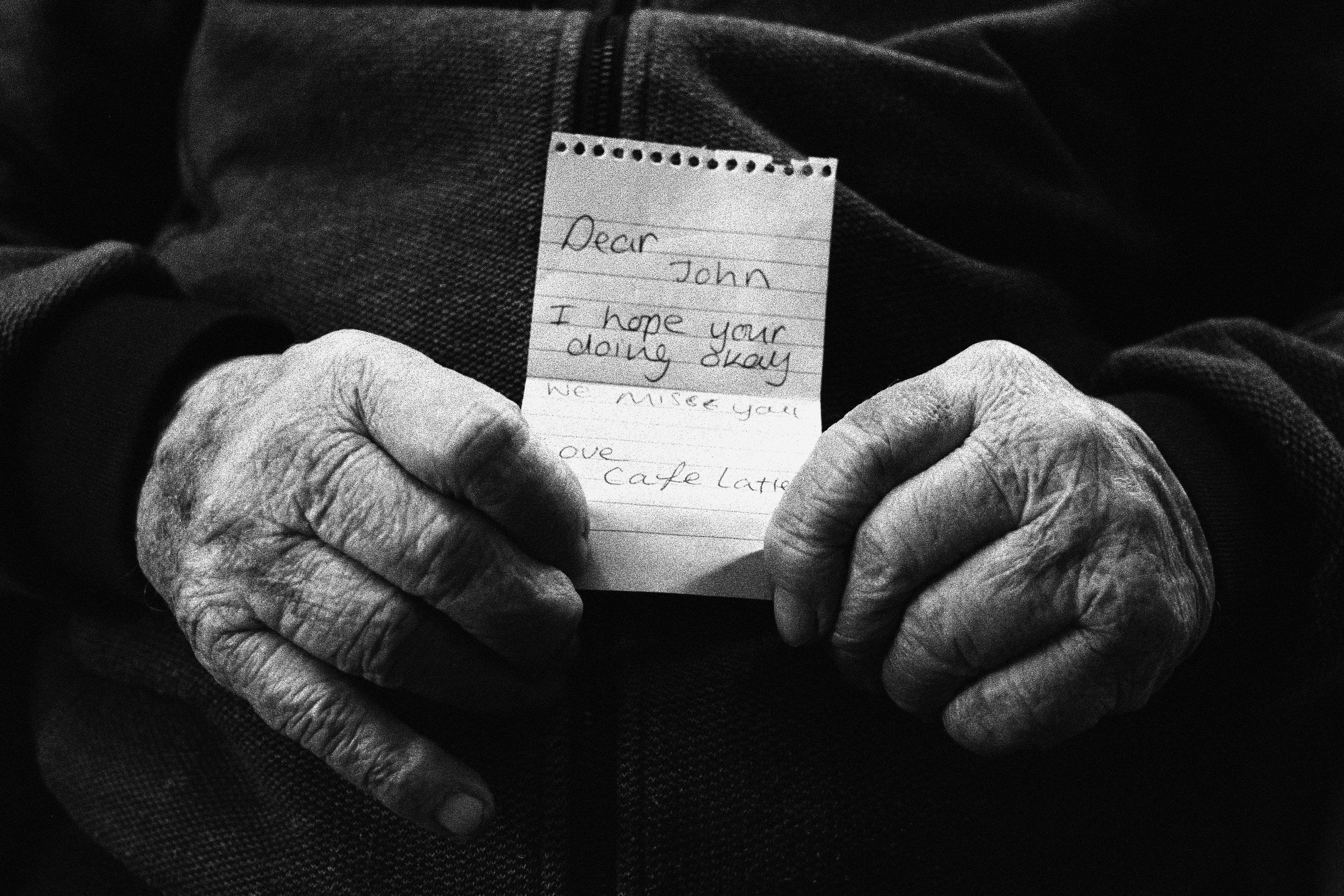 Close-up of elderly person's hands holding a small piece of paper with a handwritten note.