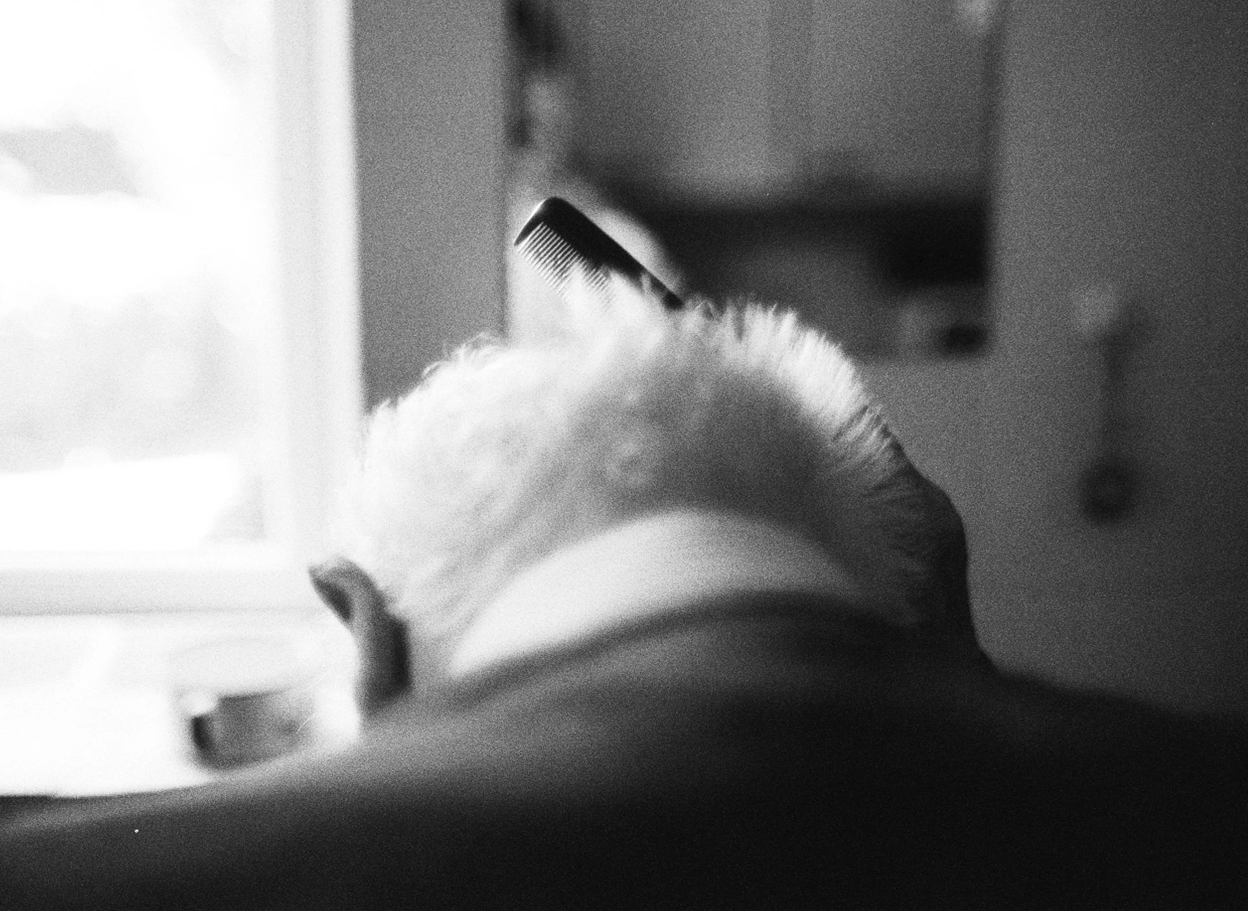 A close-up black-and-white photo of a person's hand holding a comb, with soft plush fabric visible in the background.