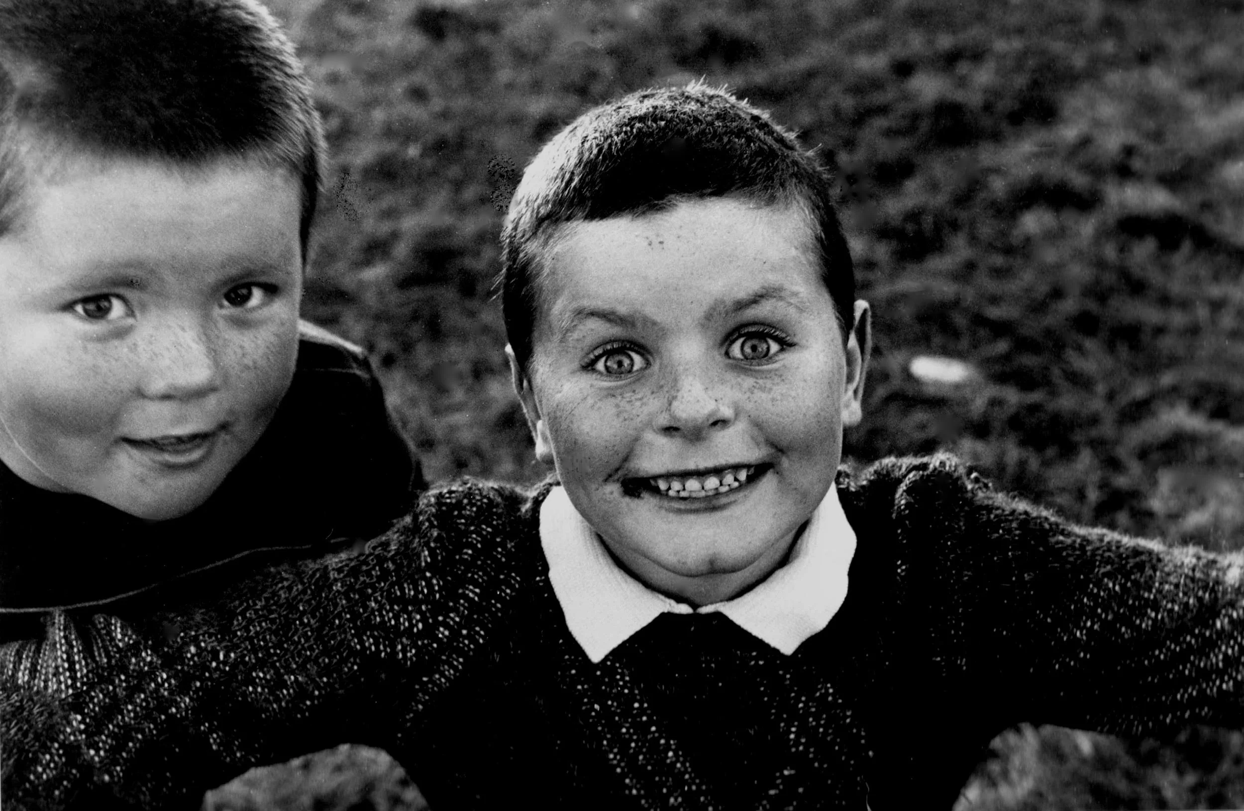 Black-and-white photo of two young boys smiling, with one in focus and the other slightly out of focus on the left.
