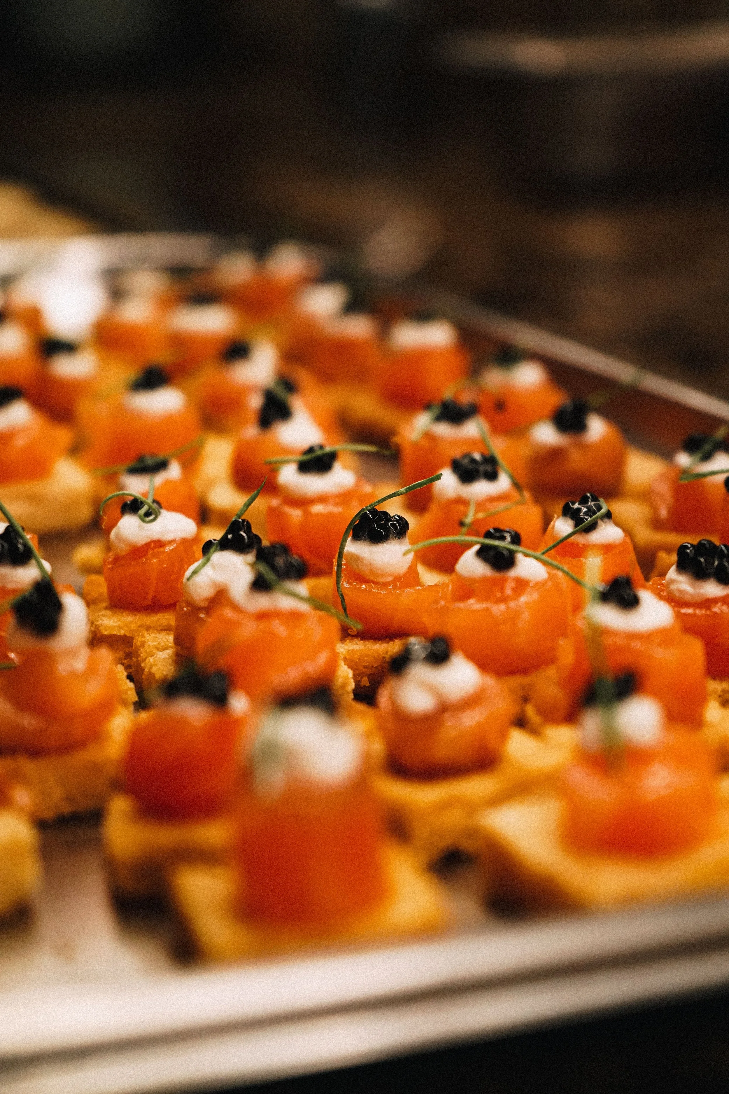 Close-up of bite-sized appetizers with smoked salmon, cream cheese, and black caviar garnished with microgreens on a tray.