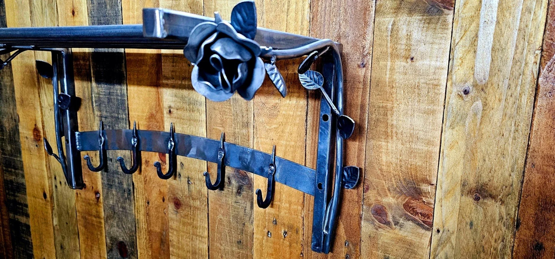 Black metal wall-mounted coat rack with decorative leaf accents and hooks, mounted on a wooden wall.
