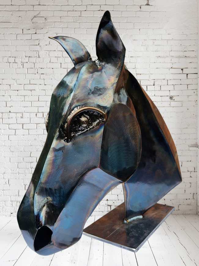 Large metal sculpture of a horse's head set against a white brick wall background.