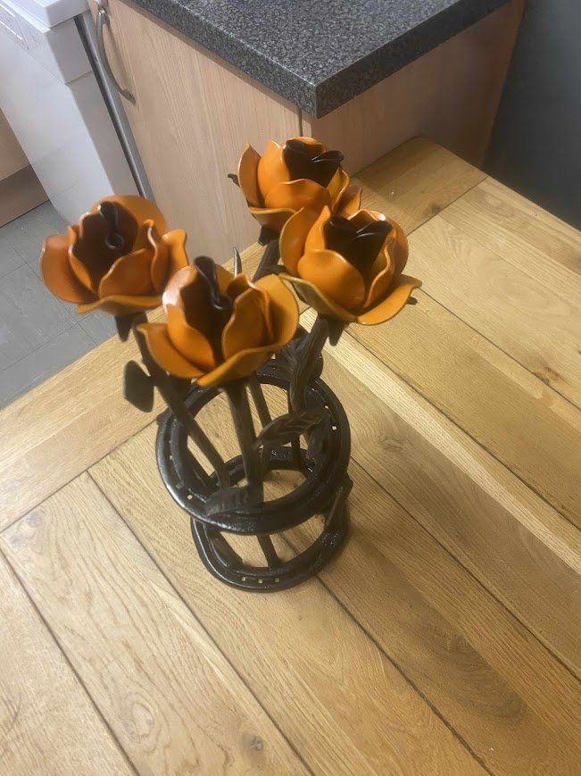 Decorative metallic orange and black flowers in a black circular wire holder on a wooden table.