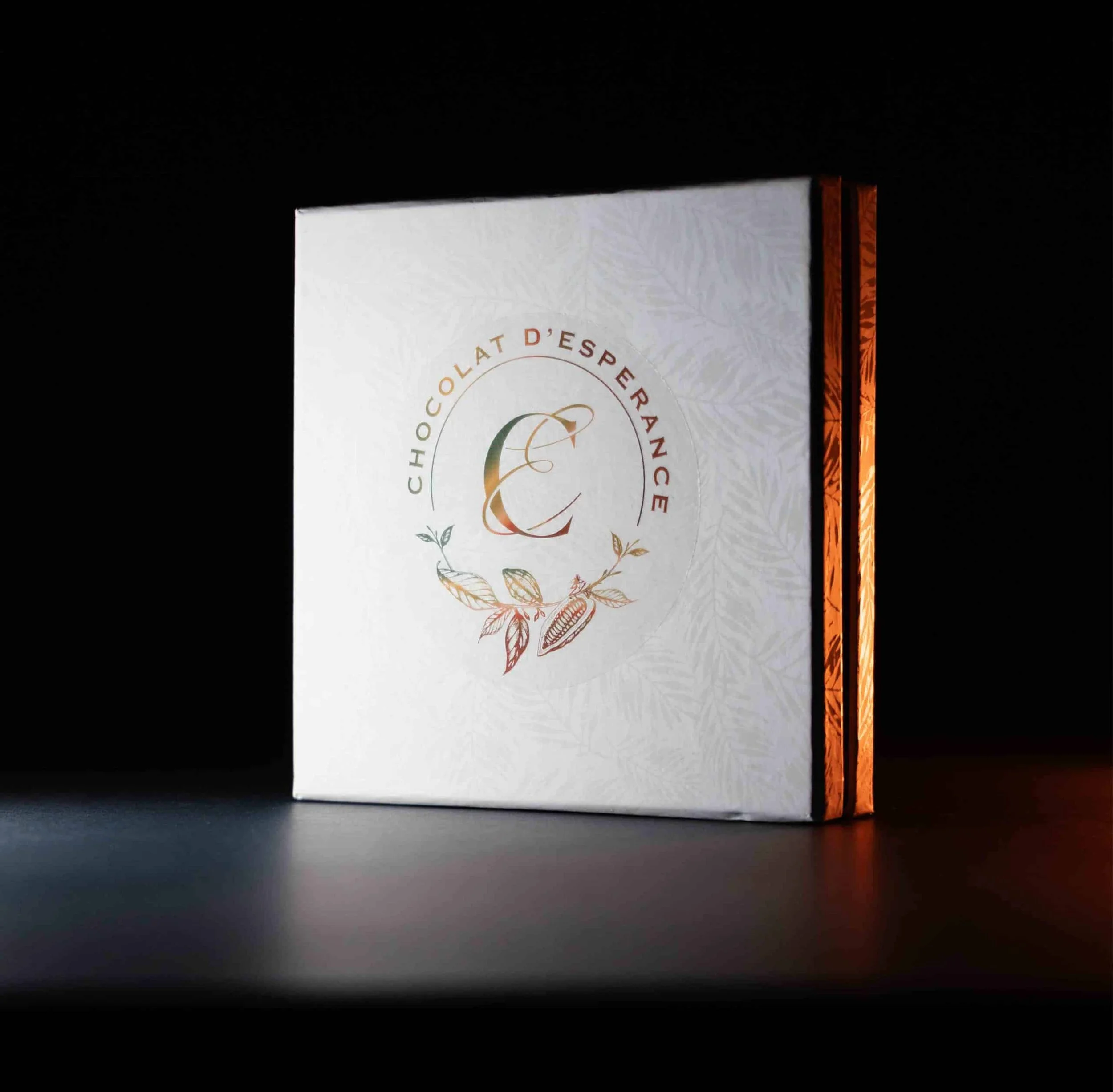 Boîte de chocolat blanc à l'orange appelée "Chocolat d'Espérance" avec un design blanc, ornement de feuilles et inscription en français.