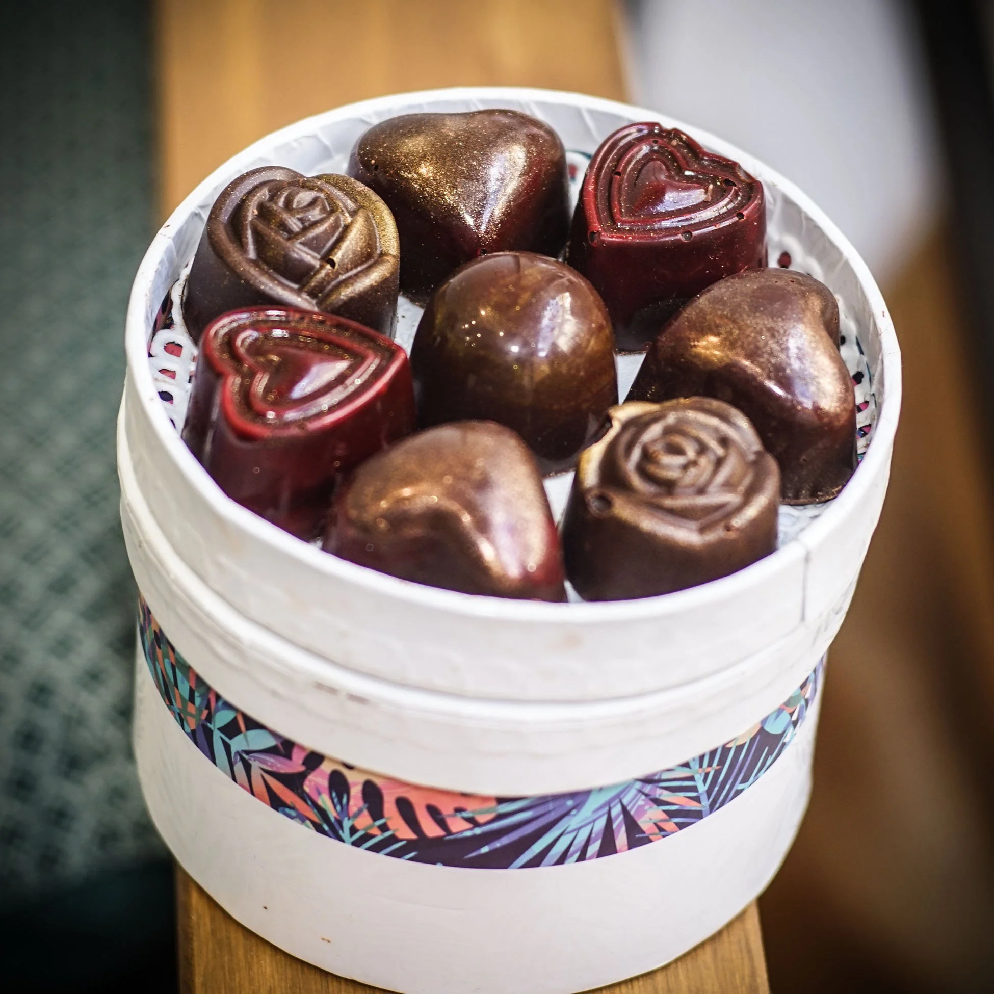 Bonbons en forme de cœurs et ronds, dans une boîte ronde blanche avec un motif coloré, sur une surface en bois.