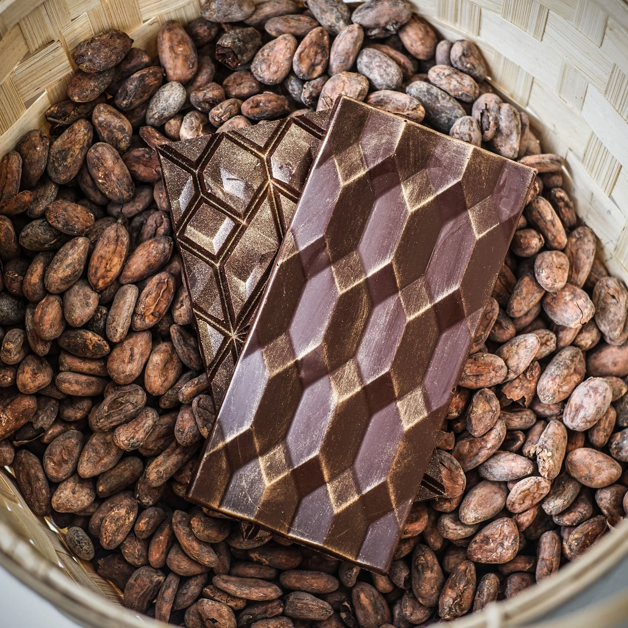Deux barres de chocolat au lait posées sur des fèves de cacao dans un panier en osier.