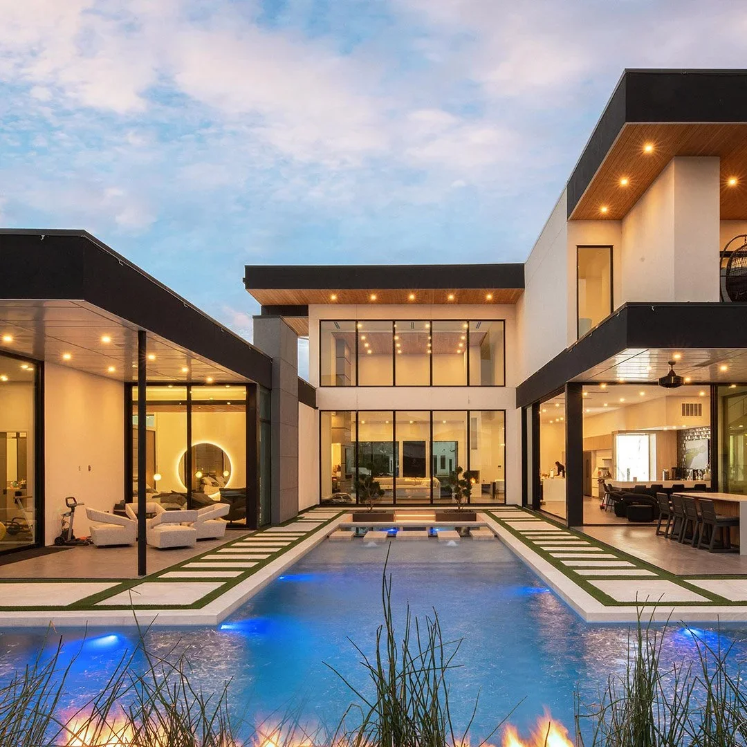Modern two-story house with large glass windows and outdoor pool, landscaped backyard, and outdoor seating area at dusk.