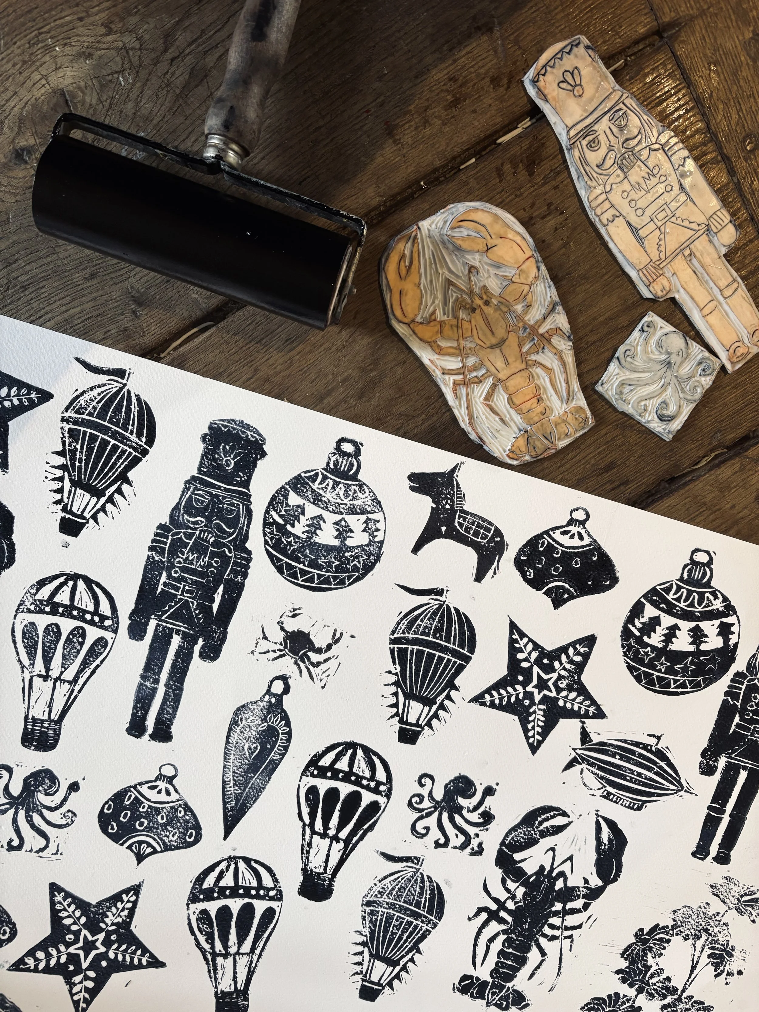 Image d'un tampon encreur, des tampons en bois décoratifs avec des motifs de Noël, et une affiche avec des illustrations de décorations de Noël, comme des ballons, des étoiles, des bonhommes en pain d'épice, un lutin, et un crabe.