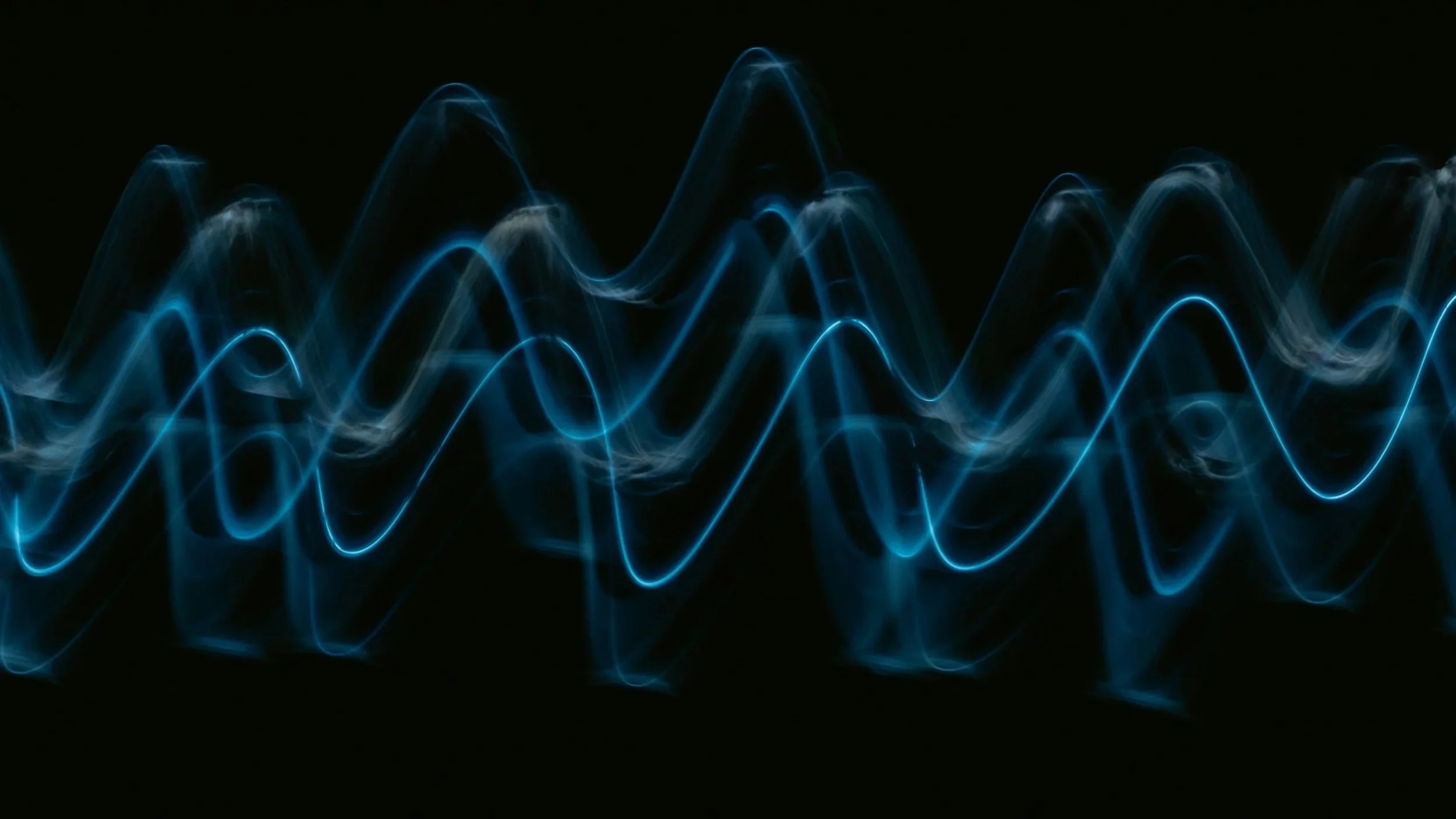 Blue light streaks on a black background resembling waves or electrical impulses.