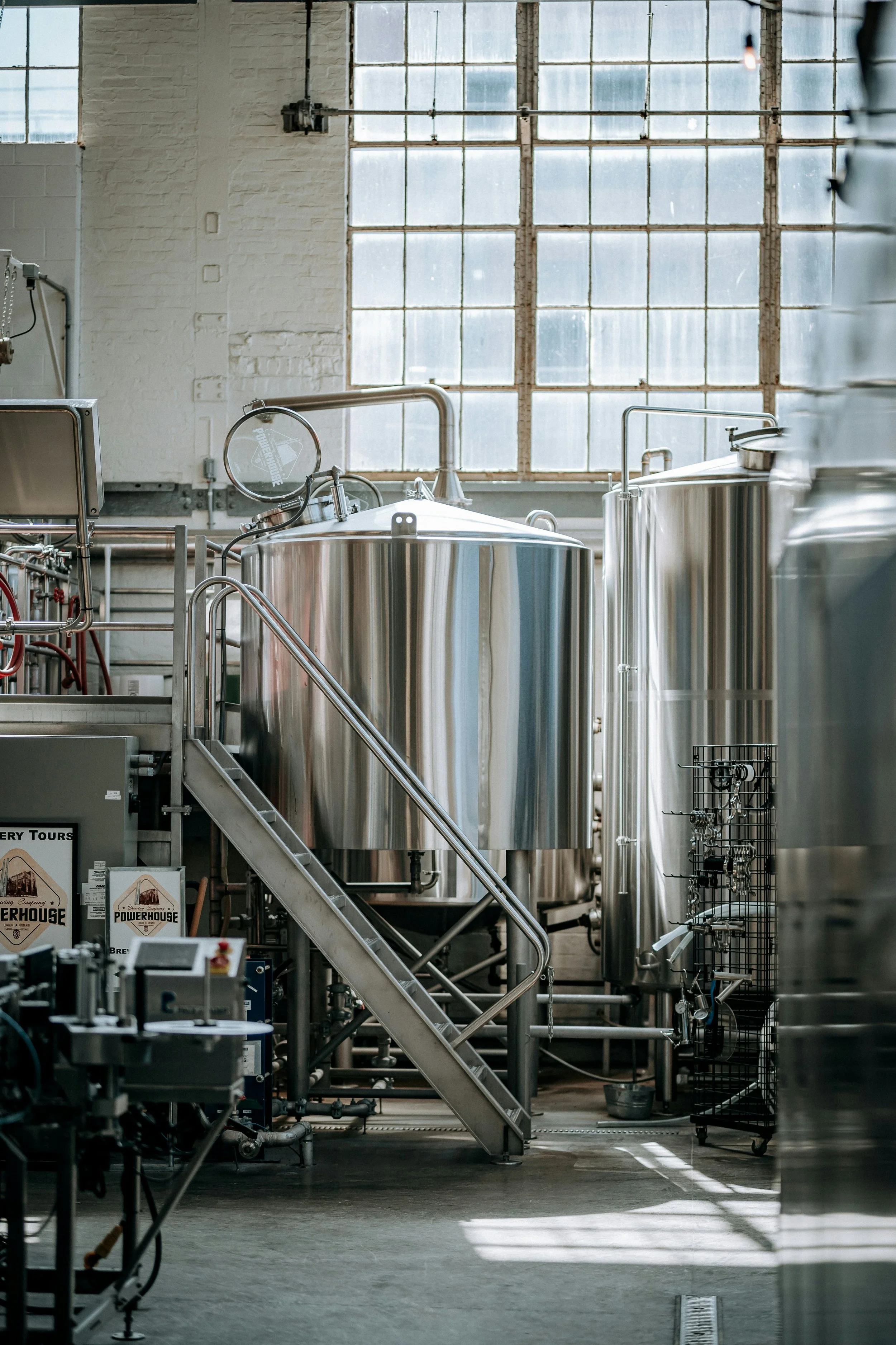 Industrial brewery with stainless steel fermentation tanks and equipment, set in a well-lit space with large windows.