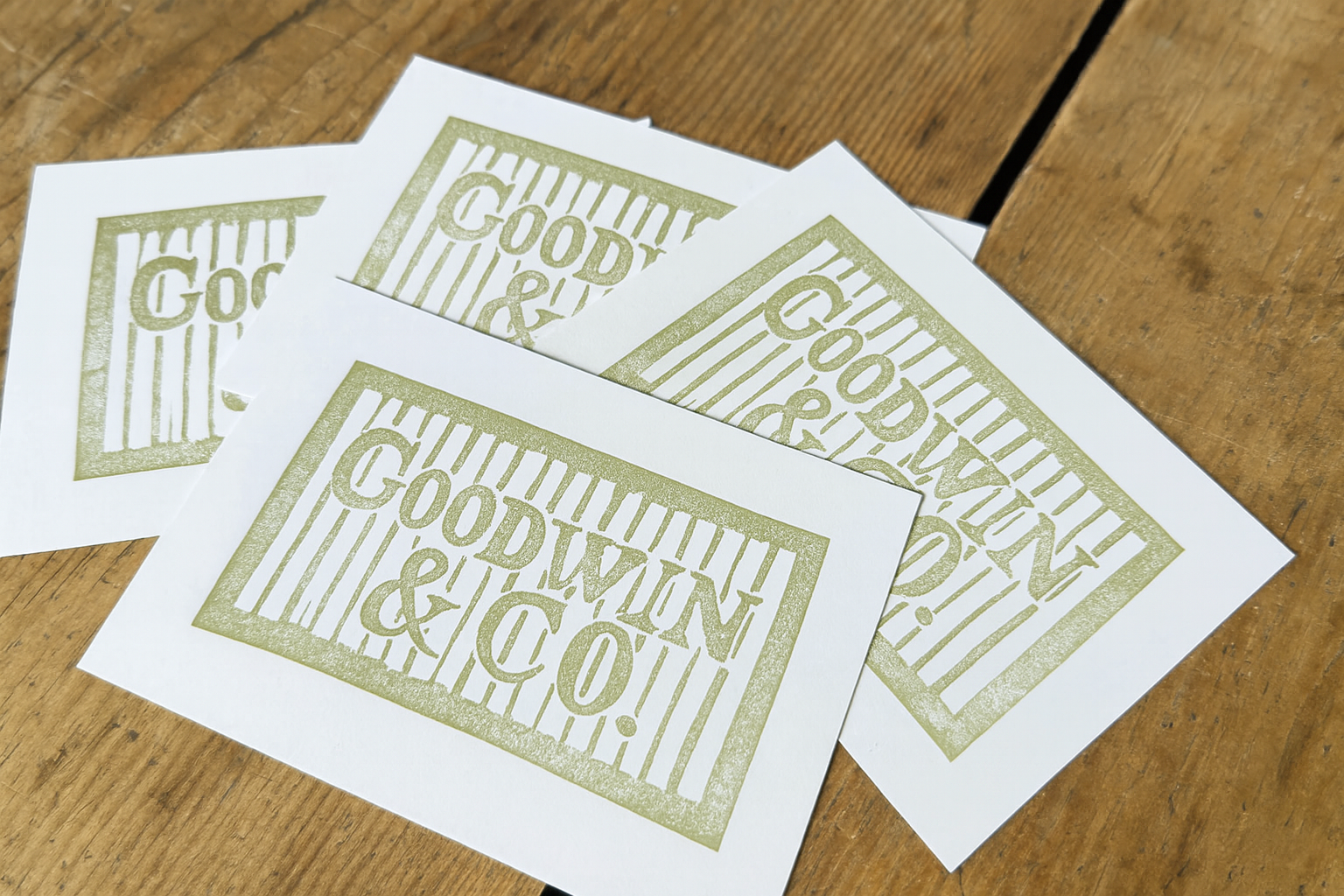 Four sheets of paper with a gold-colored design that reads "Goodwin & Co." on a wooden surface.