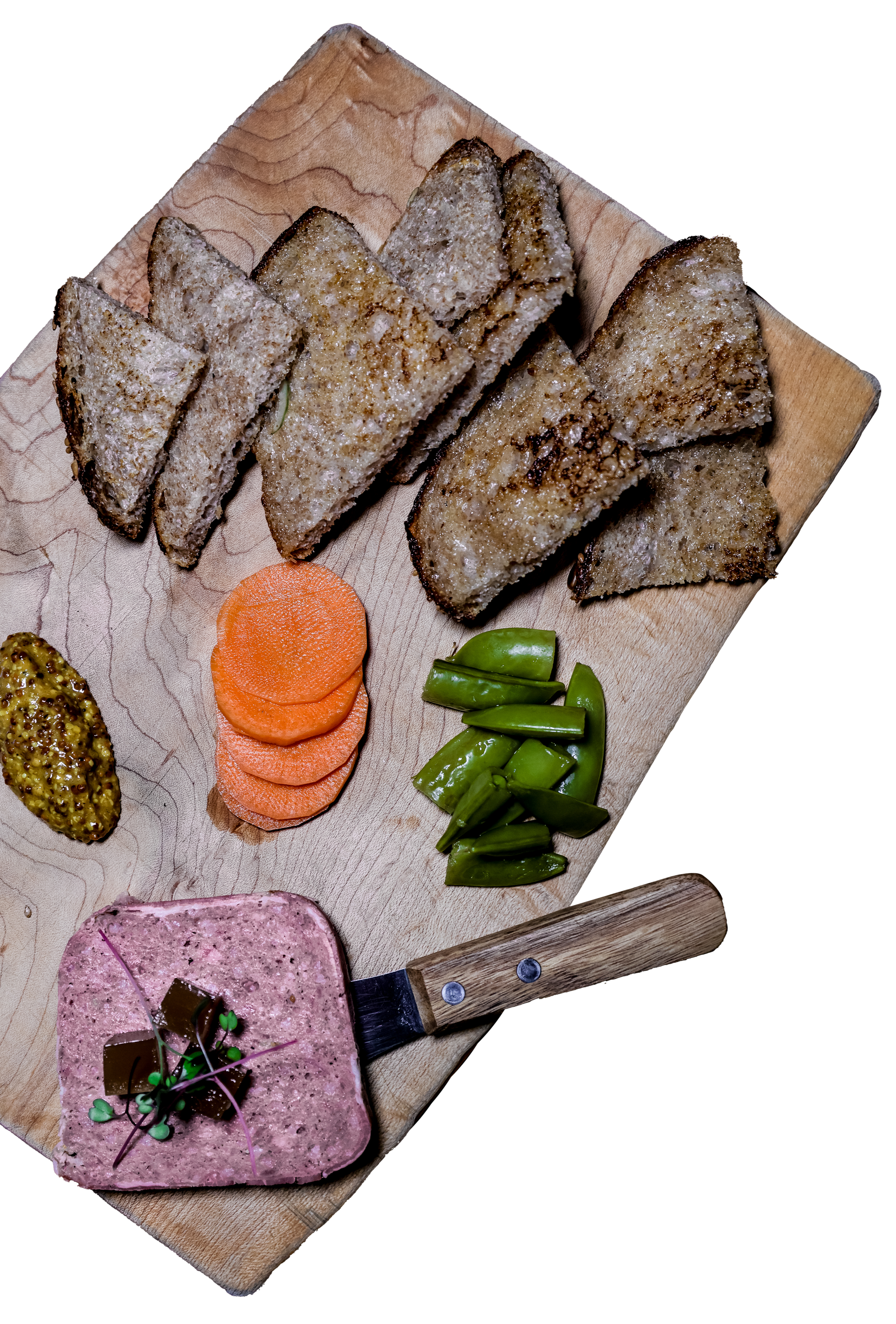 Assorted meats, vegetables, and toast on a wooden cutting board with mustard, carrots, and green peppers.