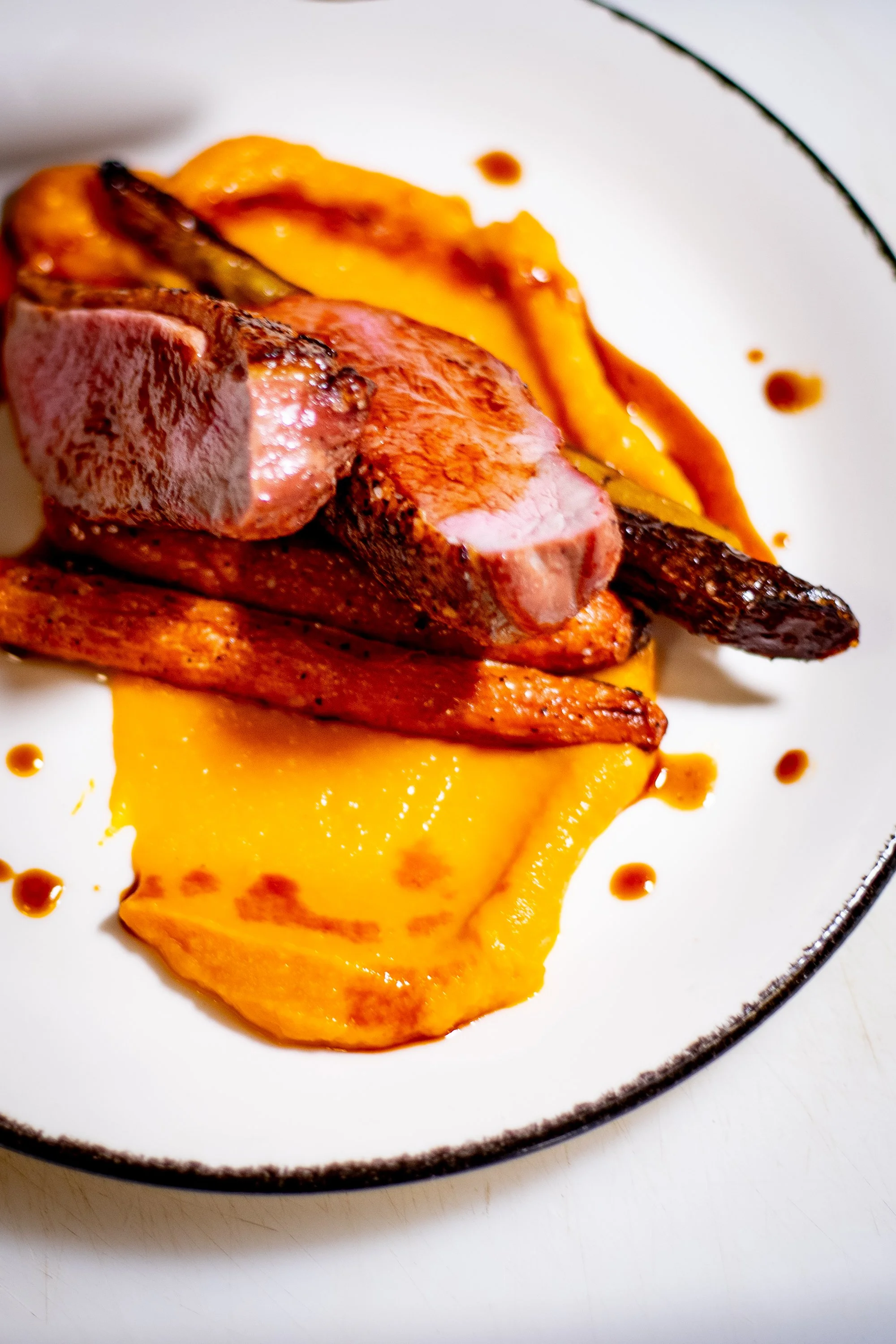 A plated dish featuring sliced meat, served over mashed sweet potatoes on a white plate.