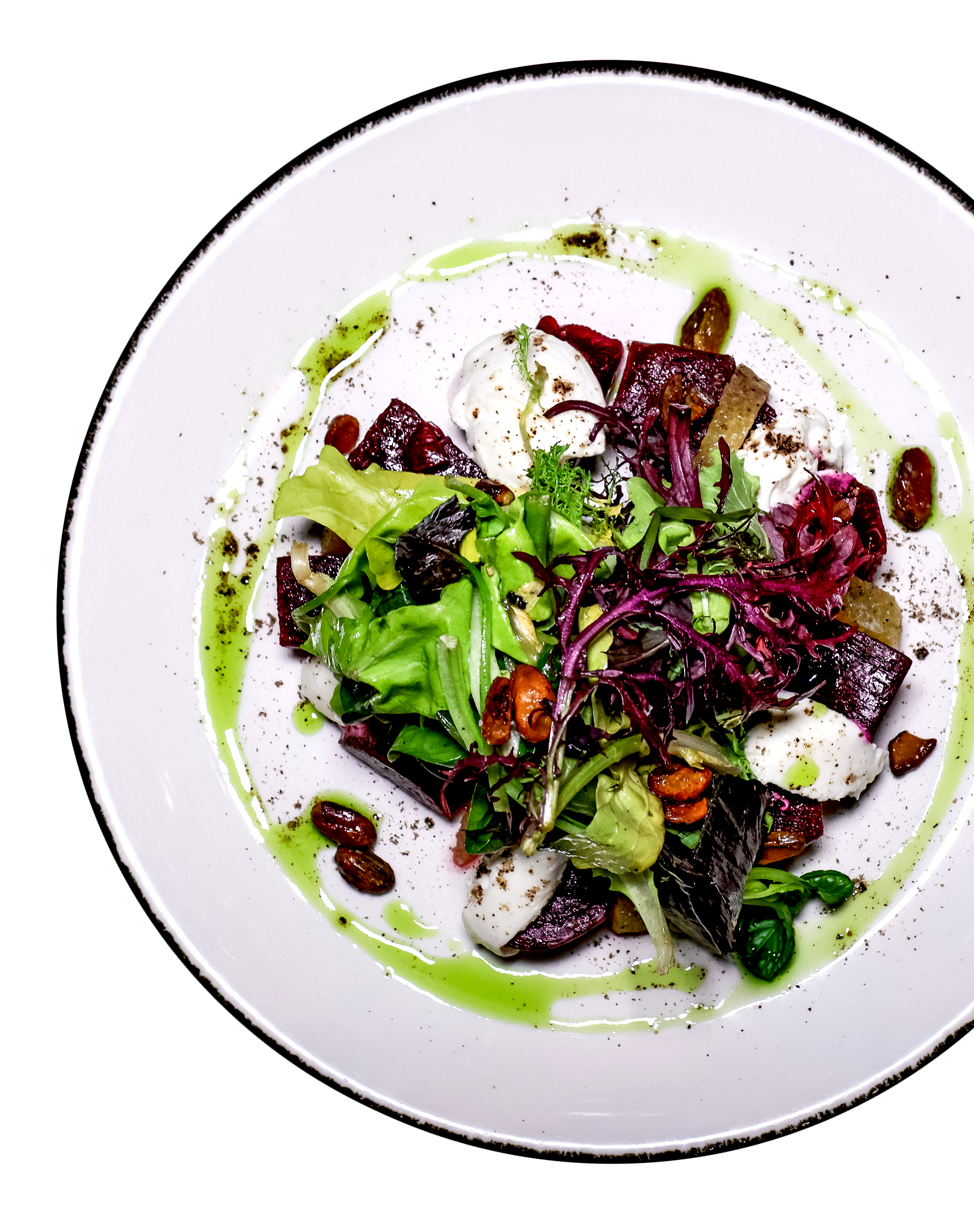 A plate of mixed greens salad with roasted beets, walnuts, and dollops of white cheese, drizzled with green dressing.