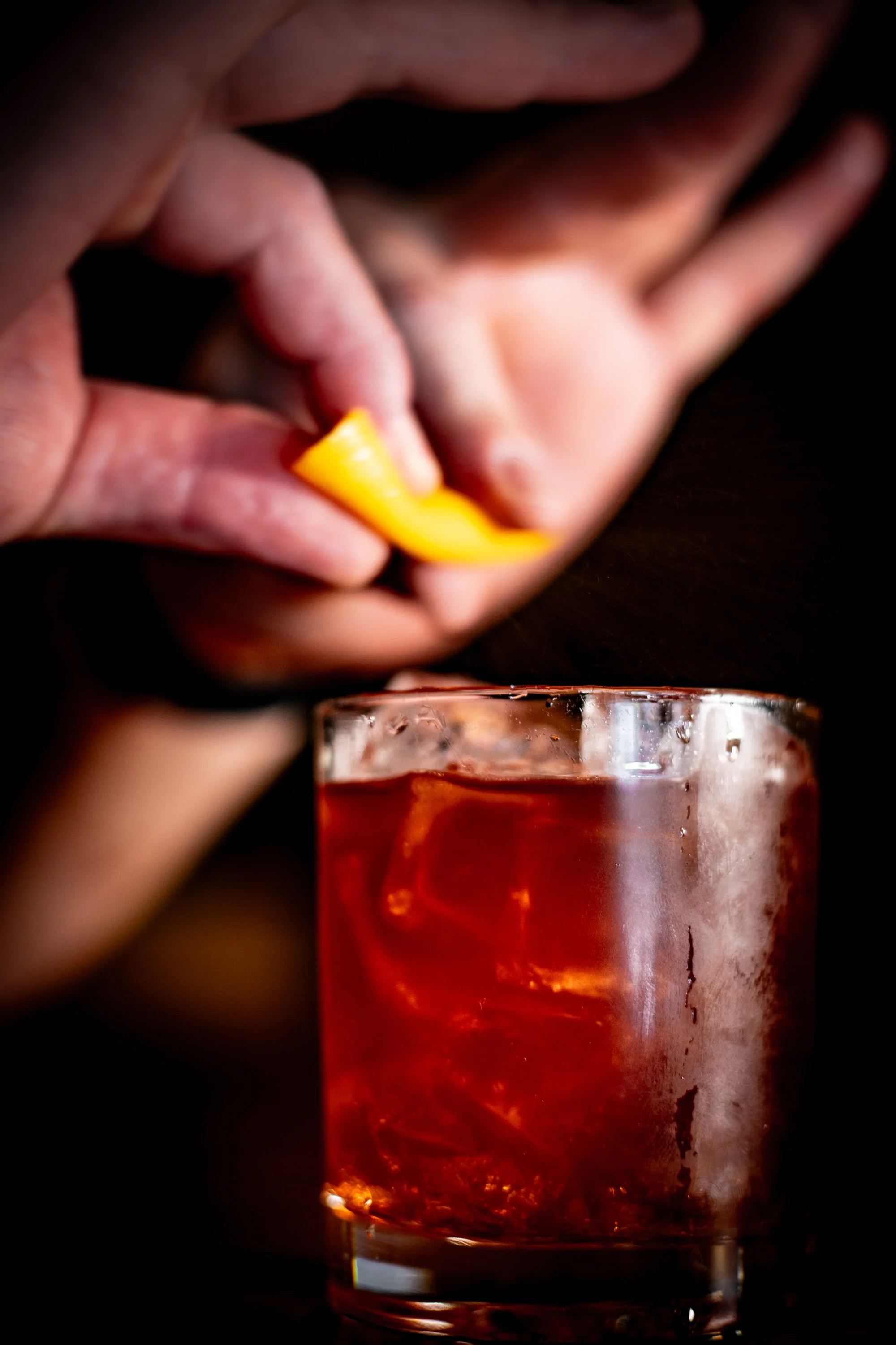 Close-up of someone squeezing a lemon slice into a glass of iced red cocktail.