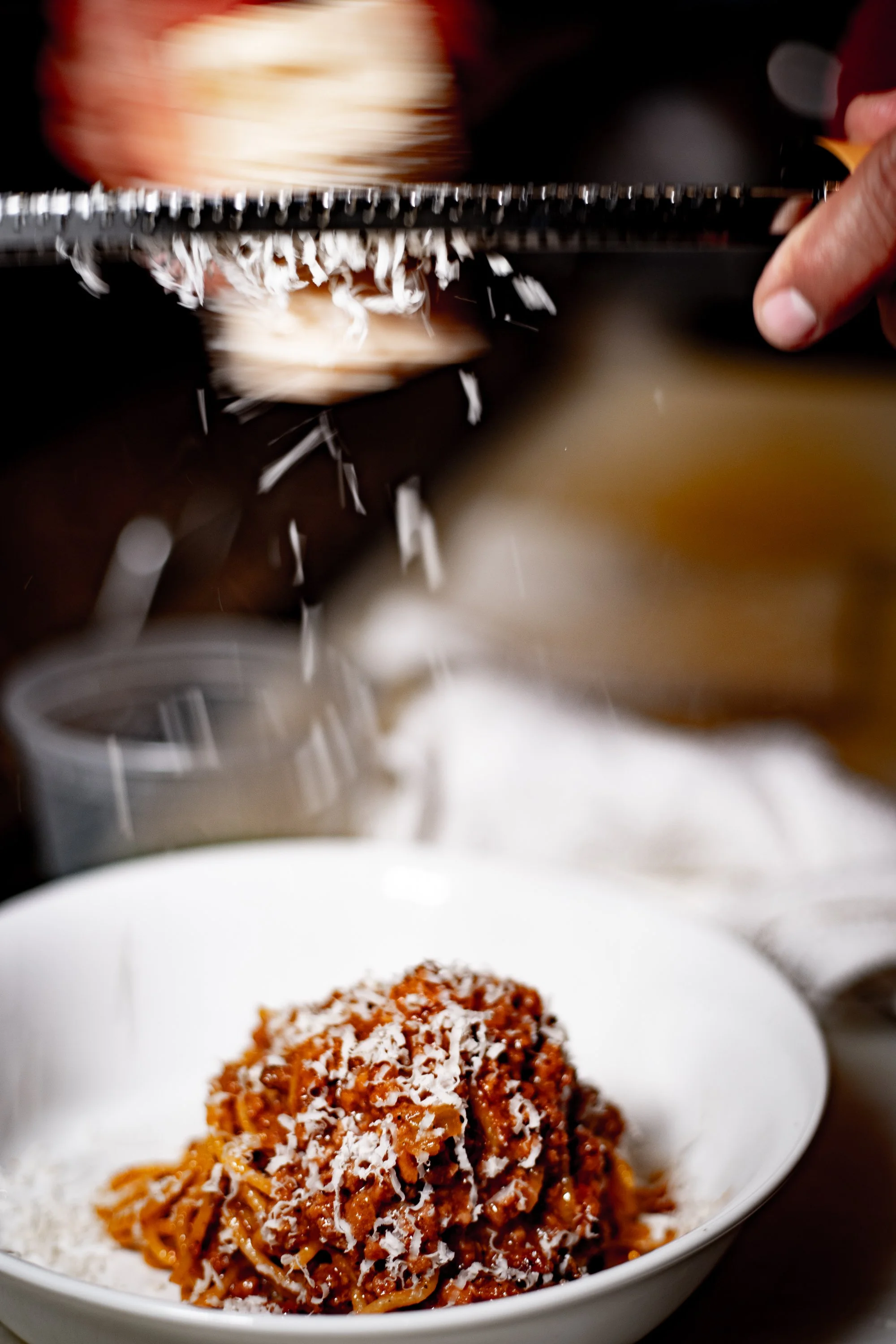 Falling grated cheese over a plate of spaghetti with sauce