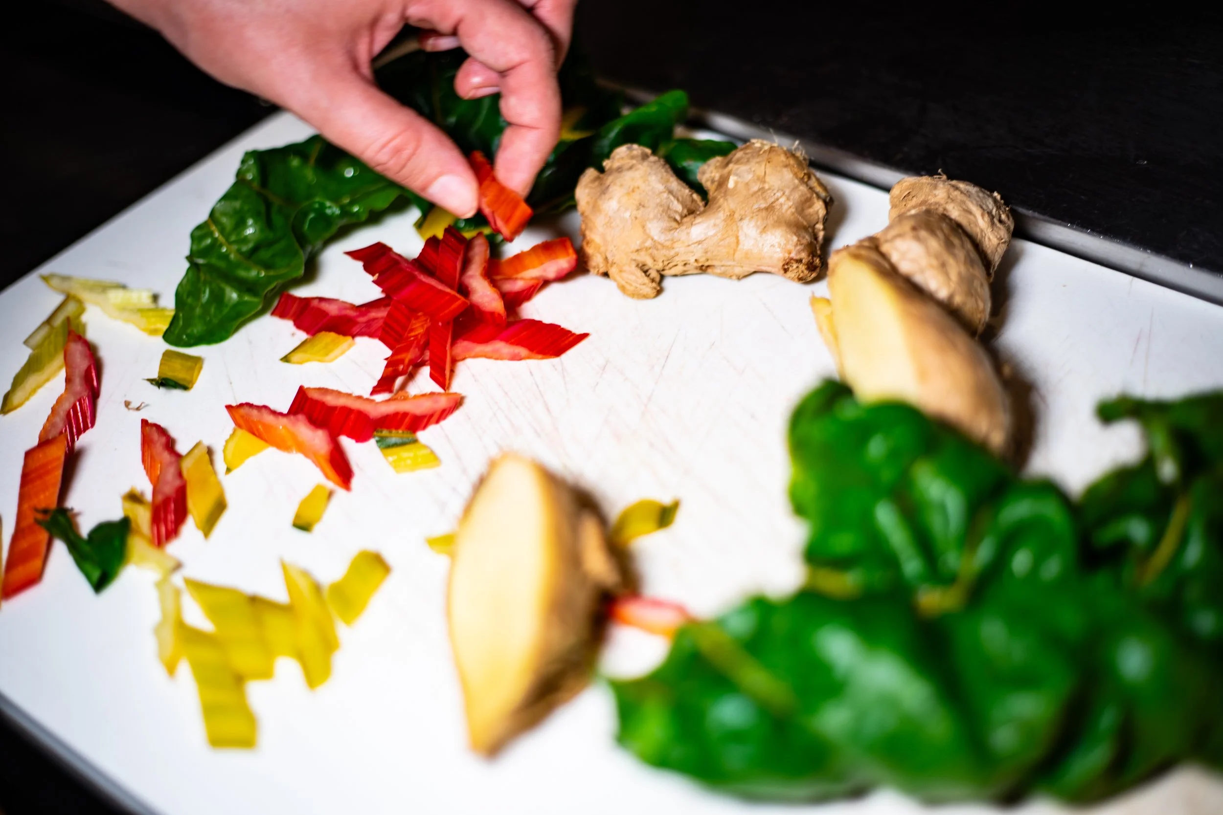 Hands chopping red, yellow, and green jalapeño peppers on a white cutting board with ginger and lemon slices nearby.
