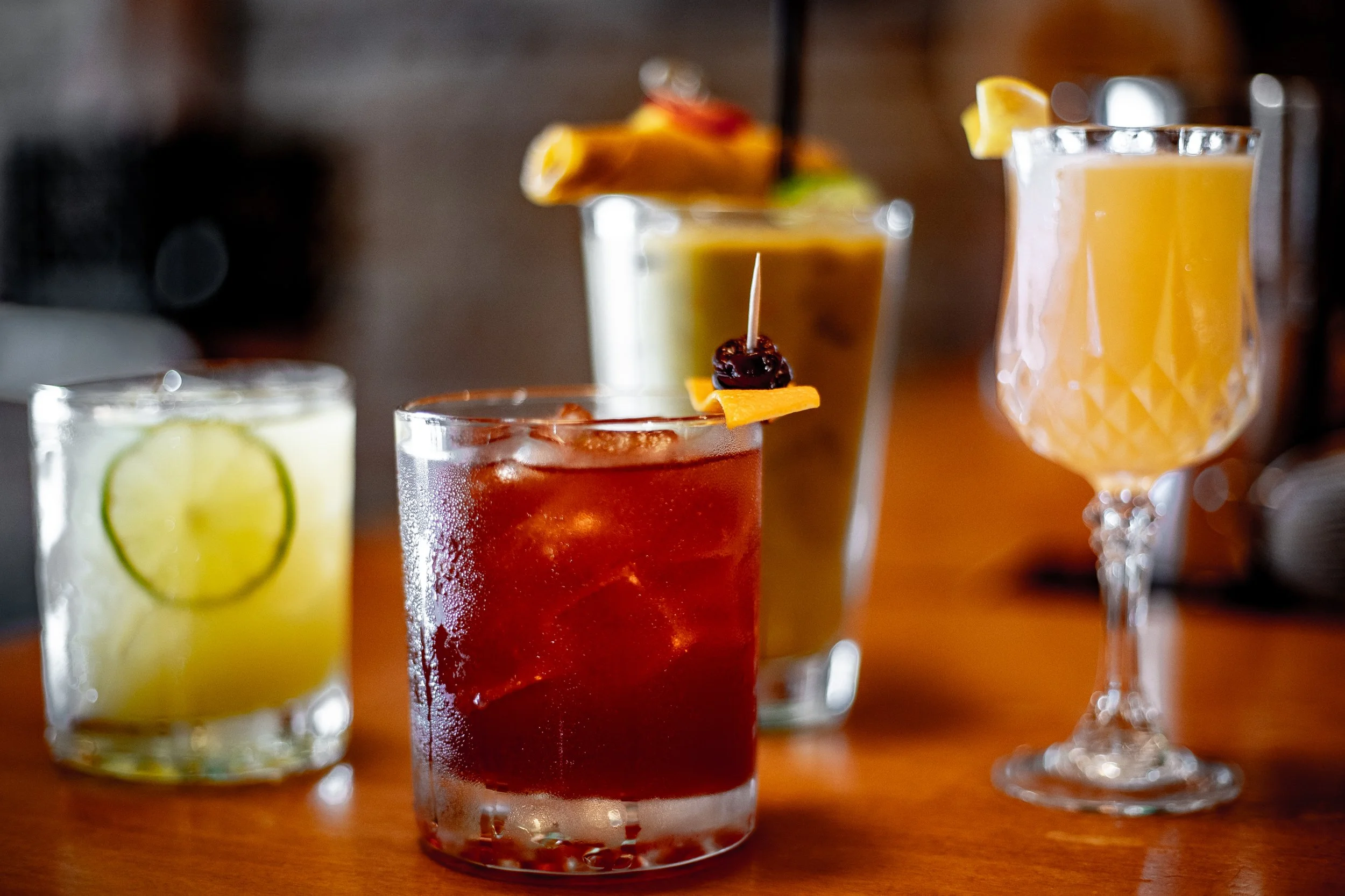 Four different colorful cocktails on a wooden table.