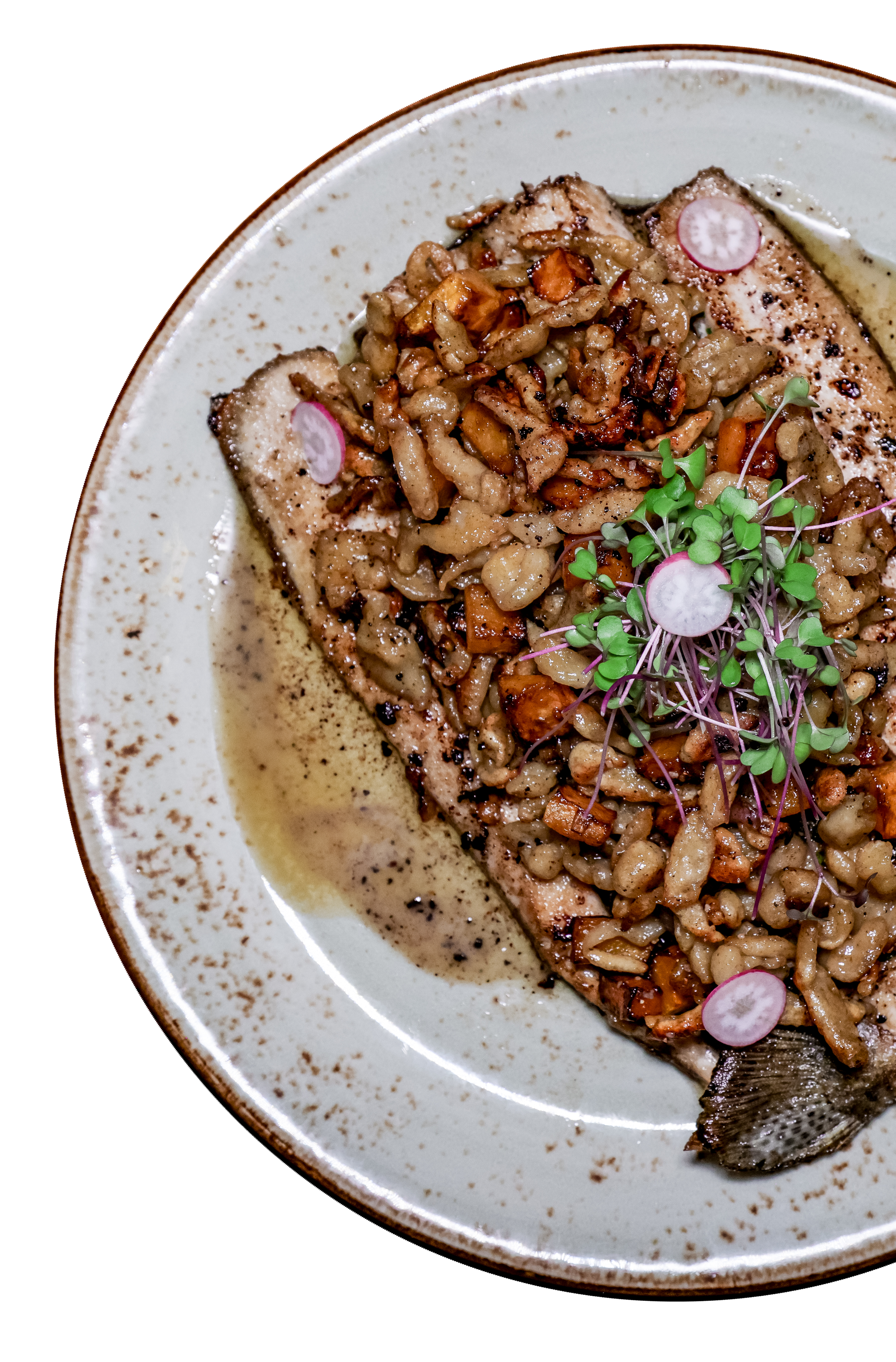 Grilled fish fillet topped with sautéed nuts and microgreens on a white plate with speckled brown border.