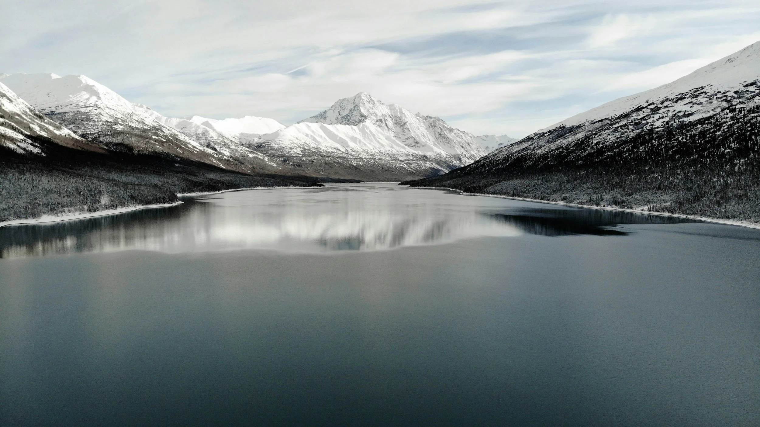 Snow-covered mountains surrounding a calm, reflective lake in a mountainous landscape.