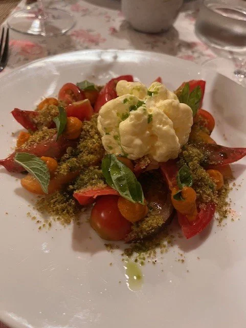 Caprese salad with cherry tomatoes, basil leaves, mozzarella, and green pesto crumbles, garnished with a dollop of burrata cheese and drizzled with olive oil at La Radice in Roccaverano.