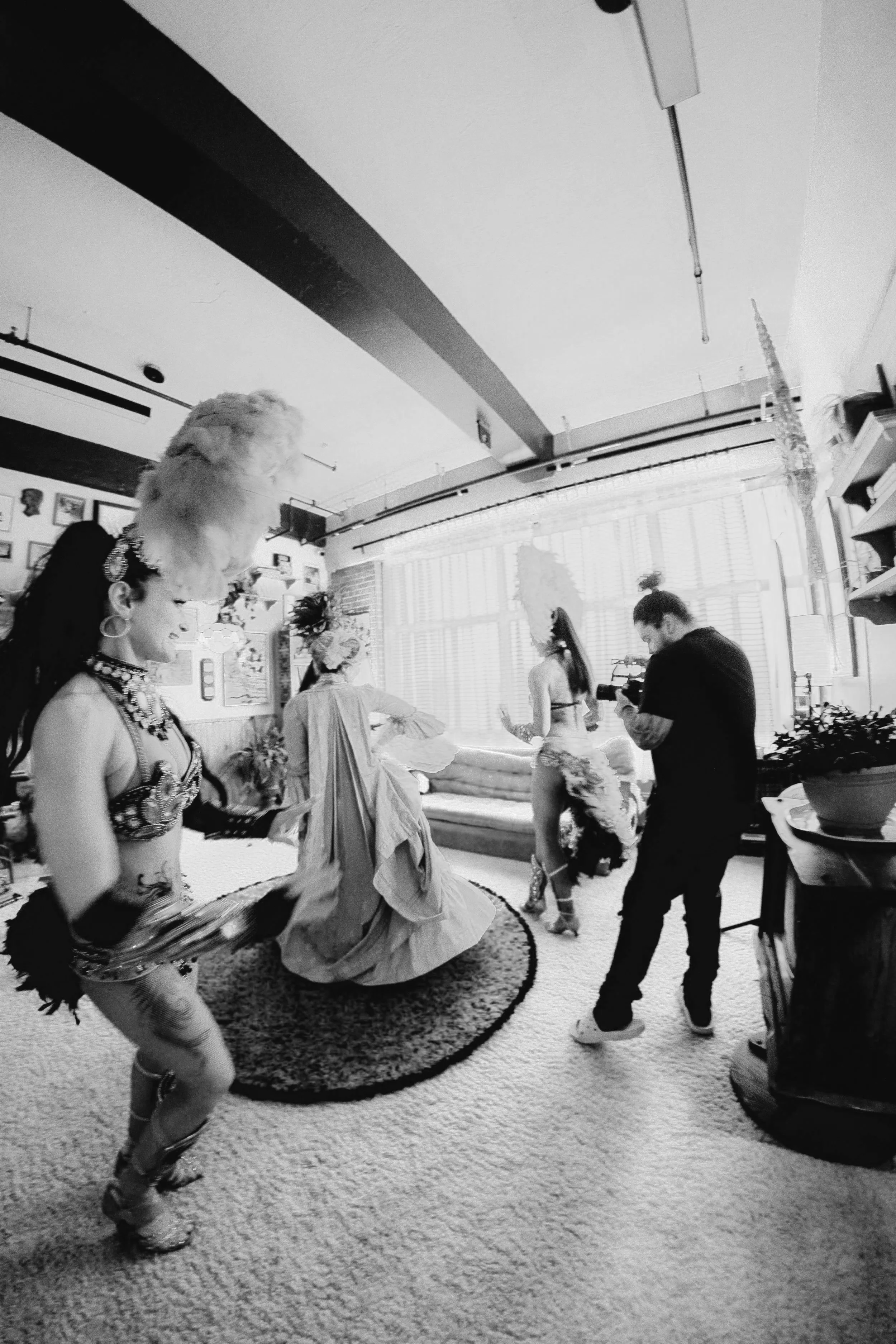 People dancing and a photographer capturing the scene in a cozy, well-lit room decorated with paintings and plants.
