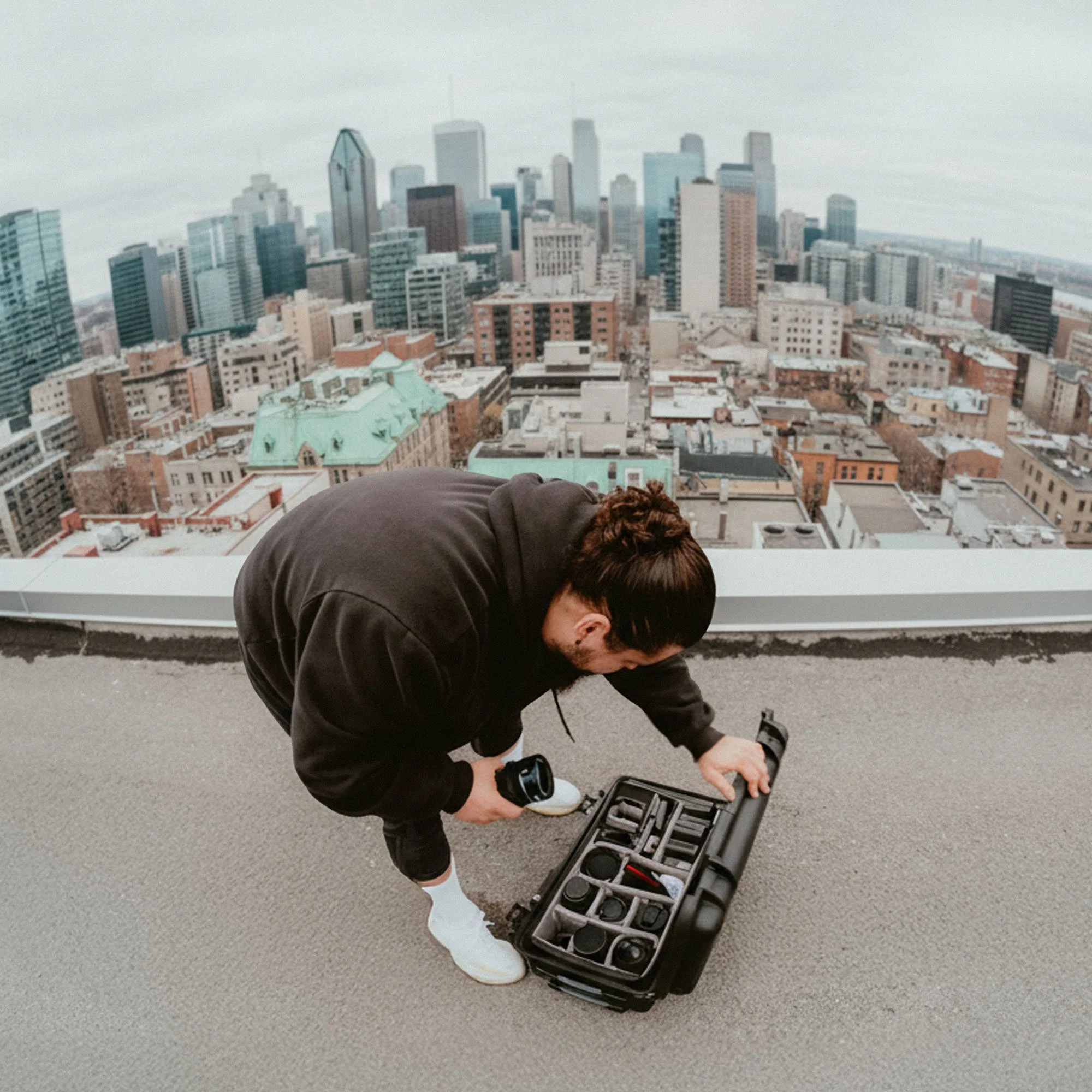 Person kneeling on rooftop with city skyline in background, examining equipment in a black case.