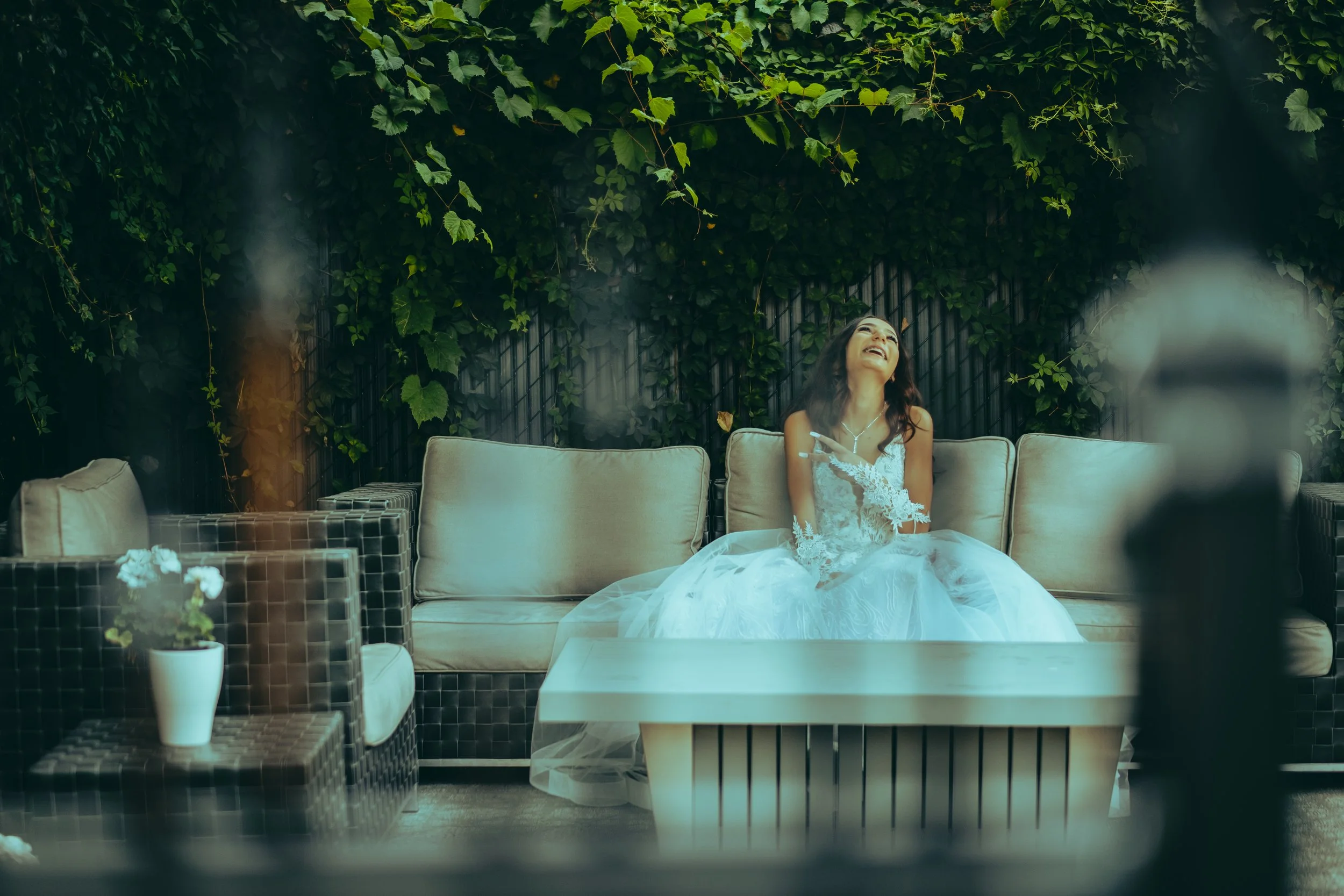 Videographer in Montreal capturing professional music videos, corporate videos, and live events. High-quality video productionA woman in a wedding dress sitting on an outdoor sofa, laughing and looking up, surrounded by greenery and casual furniture.