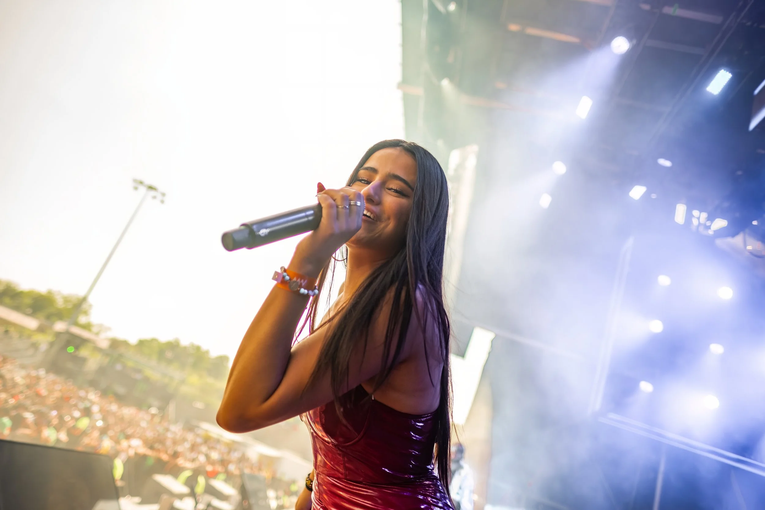 Videographer in Montreal capturing professional music videos, corporate videos, and live events. High-quality vidA woman singing into a microphone on stage at an outdoor concert, smiling with a large crowd in the background and stage lights overhead.