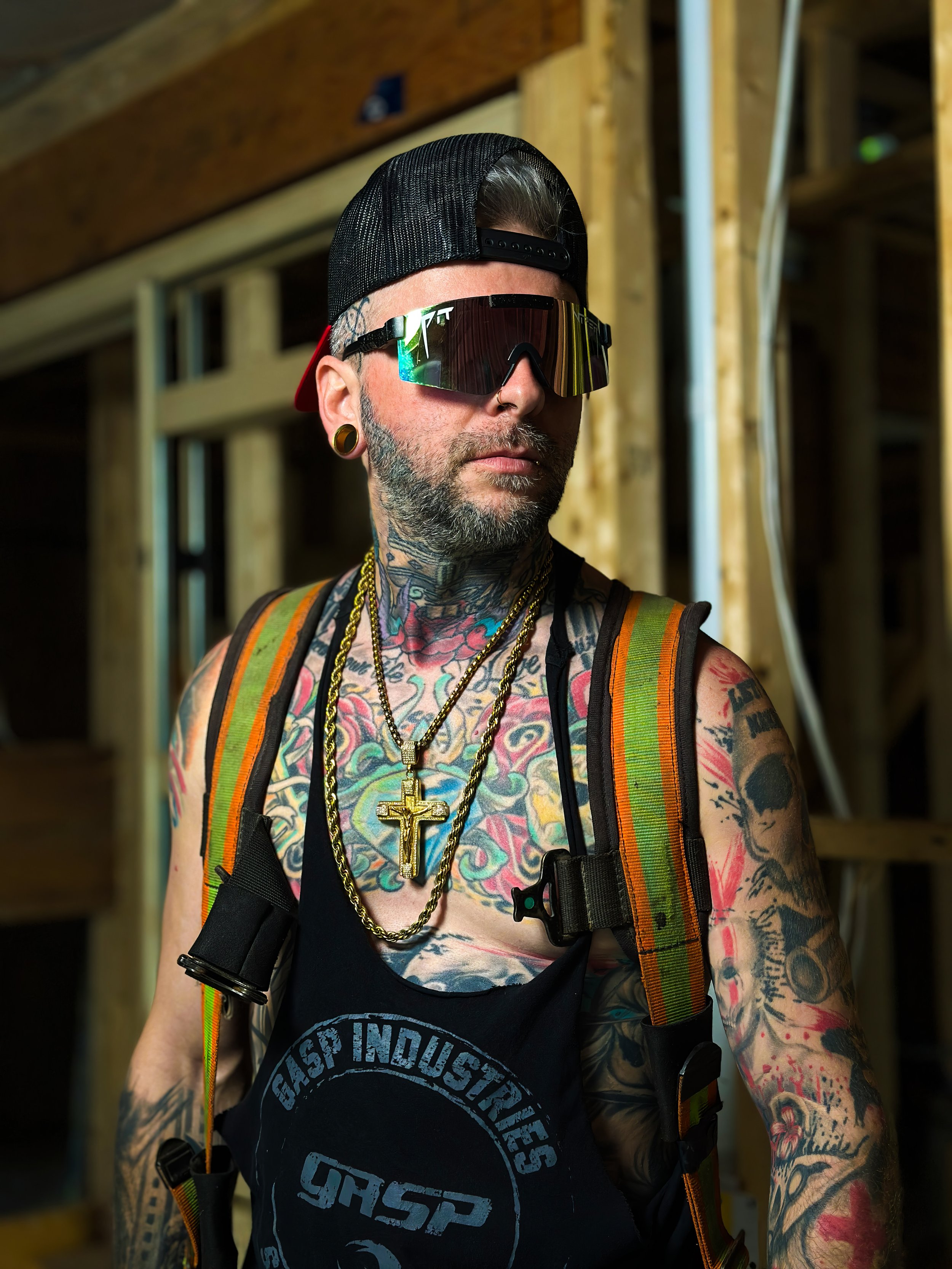 Videographer in Montreal capturing professional music videos, corporate videos, and live events. High-quality video prTattooed man wearing sunglasses, a black baseball cap backwards, a black tank top, and a backpack inside a wooden construction site.