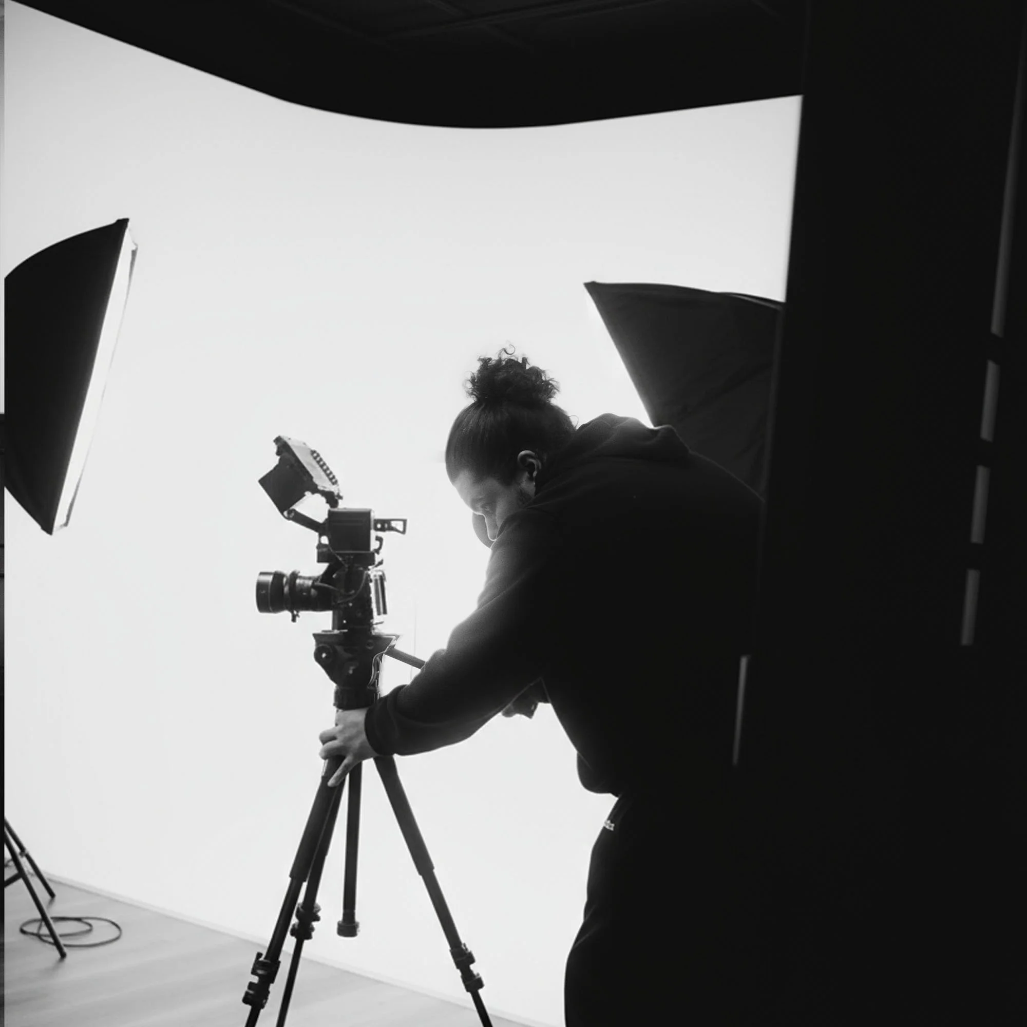 Photographer adjusting camera on tripod in a studio with lighting equipment, black and white image.
