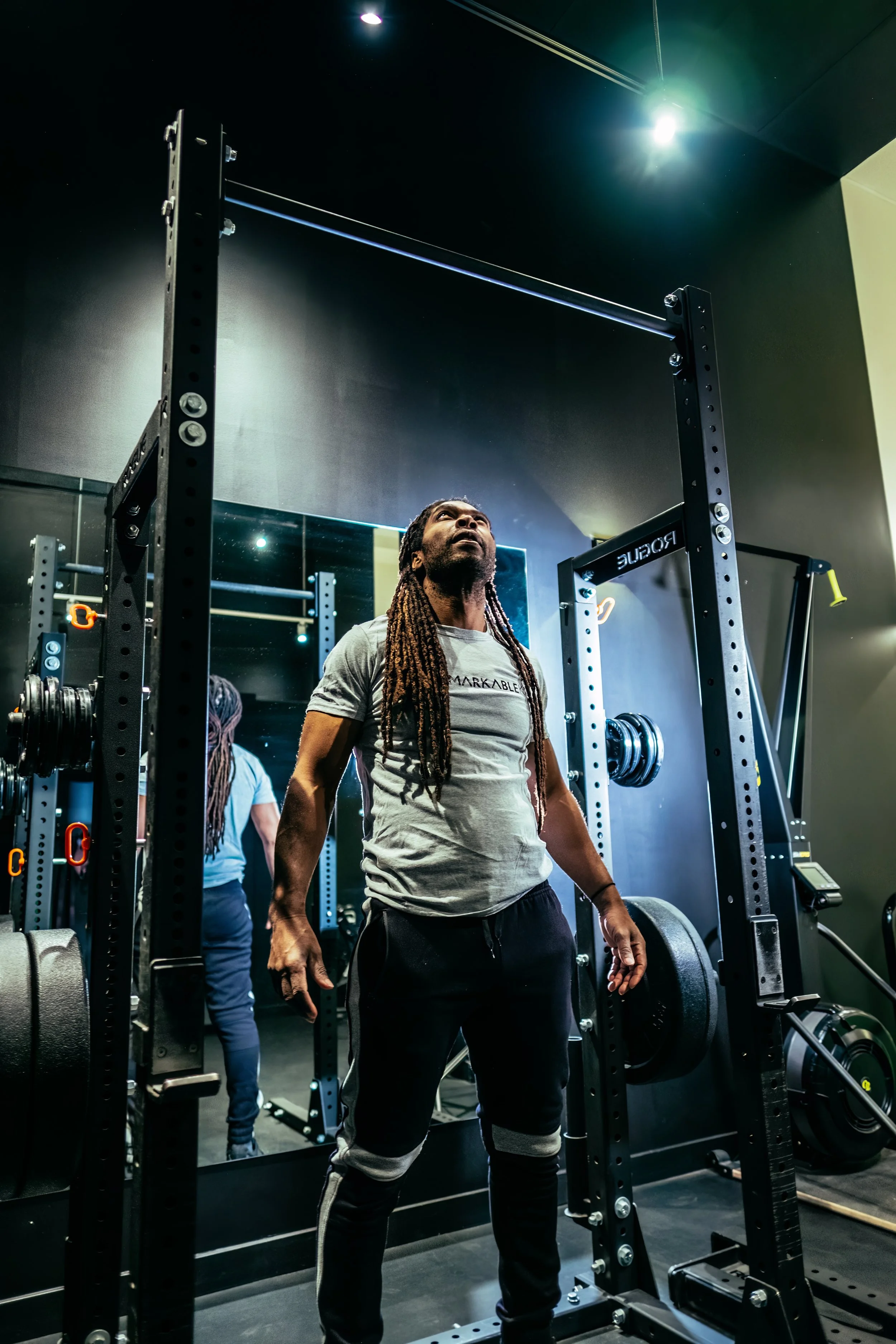Videographer in Montreal capturing professional music videos, corporate videos, and live events. High-quality video producA man with dreadlocks in a gym lifting weights, standing under a squat rack, with a mirror and another person in the background.