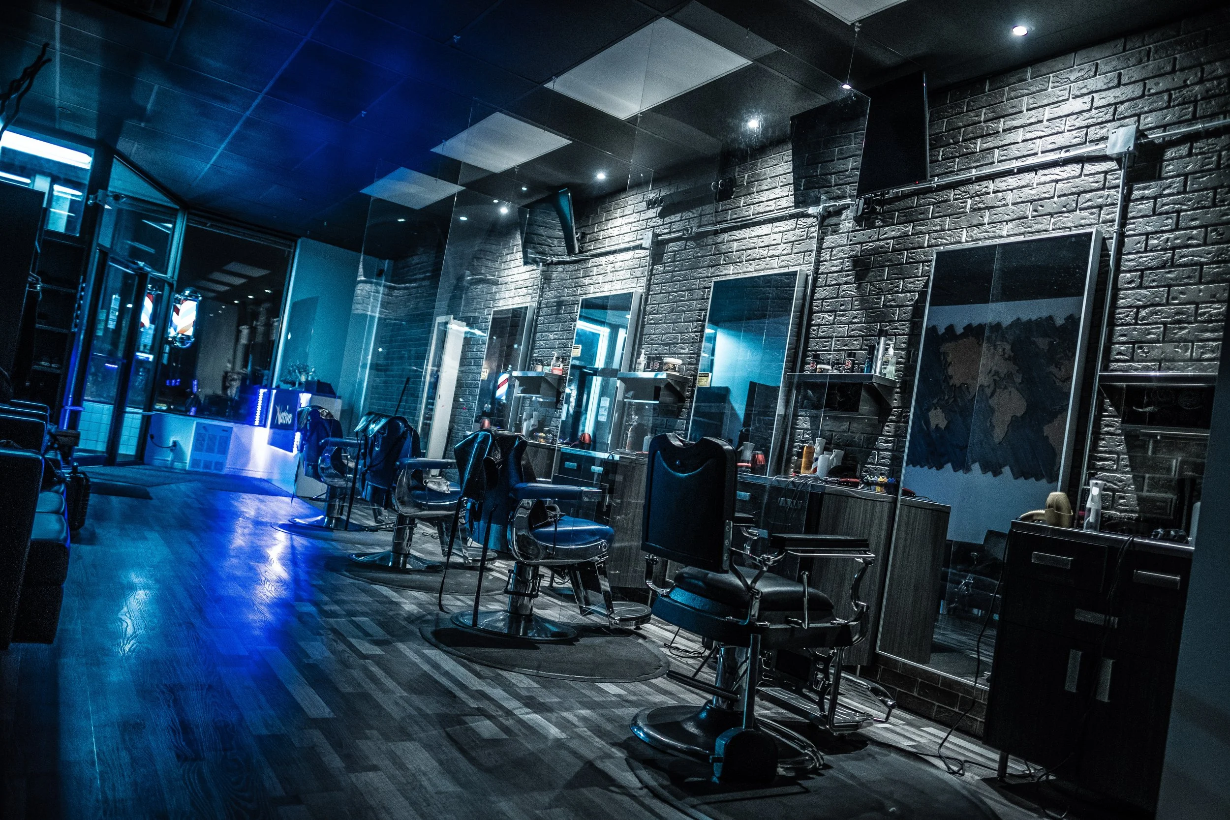 Videographer in Montreal capturing professional music videos, corporate videos, and live events. High-quality video production services Empty barbershop with chairs and mirrors, illuminated by dim blue lights, brick wall background, and wooden floor.