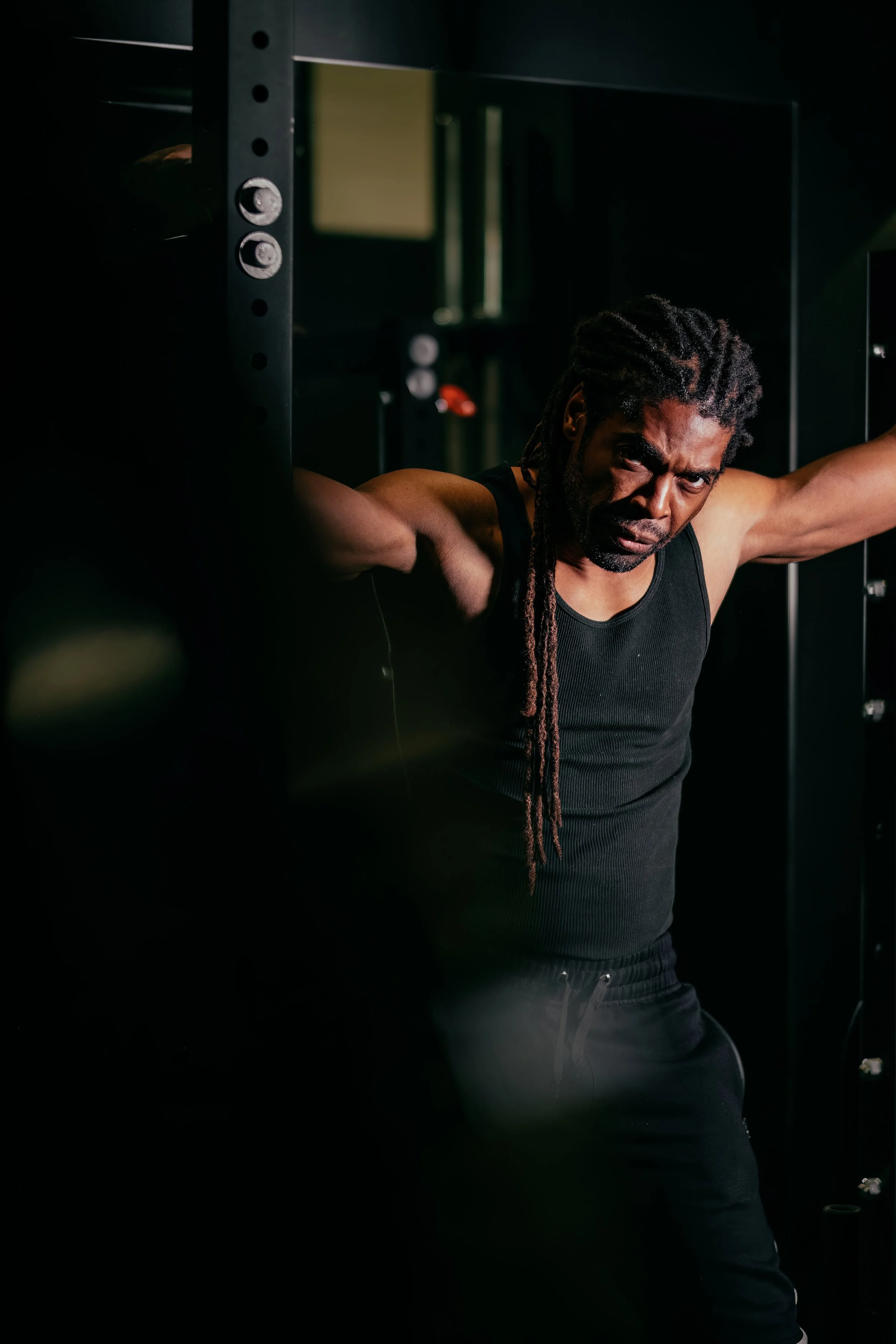 Videographer in Montreal capturing professional music videos, corporate videos, and live events. High-quality video production services in Montreal.A man with dreadlocks wearing a black sleeveless shirt is stretching in a dark gym.