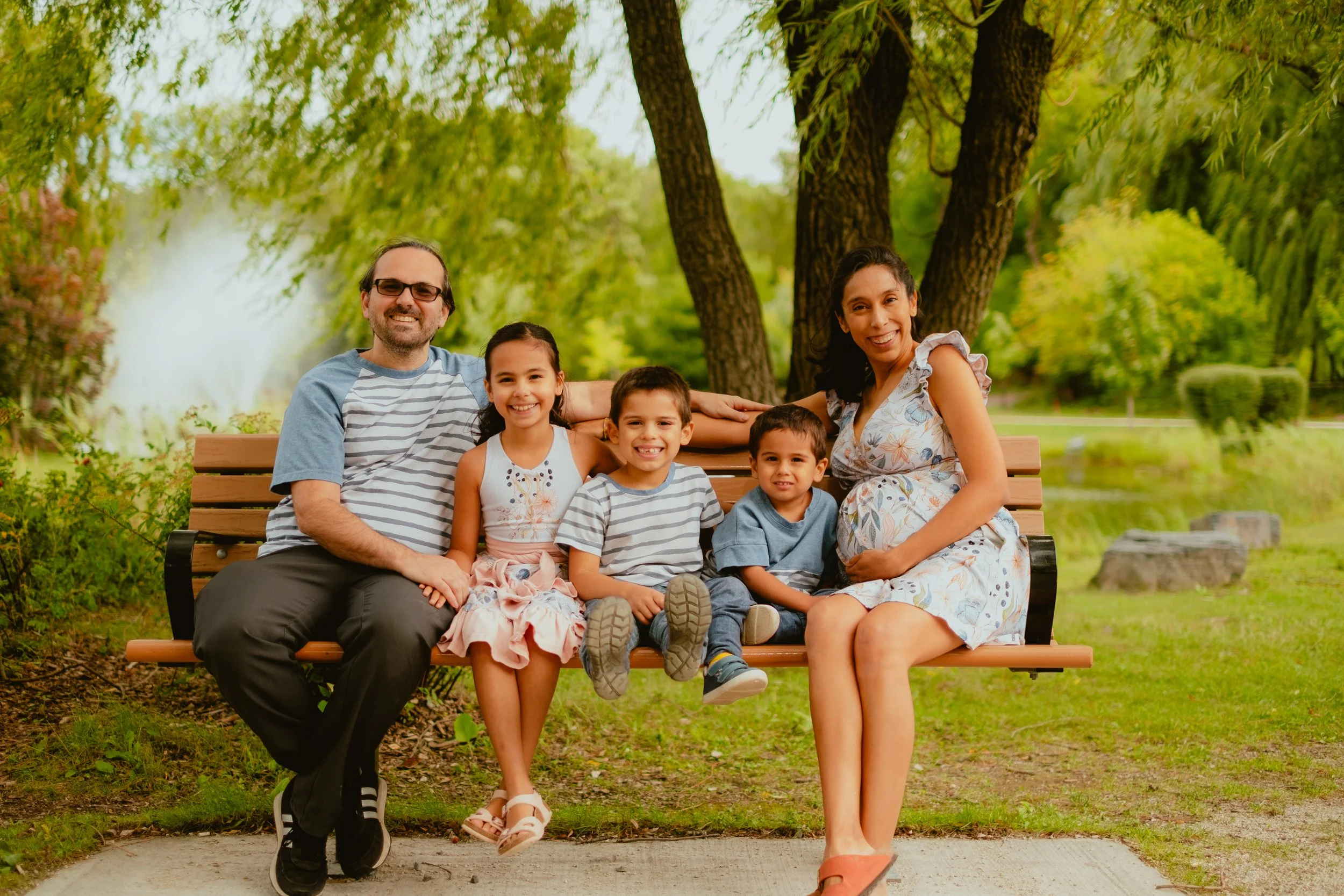 Videographer in Montreal capturing professional music videos, corporate videos, and live events. High-quality video production services in Montreal.Family of six sitting on a park bench outdoors, smiling, surrounded by green trees and grass.