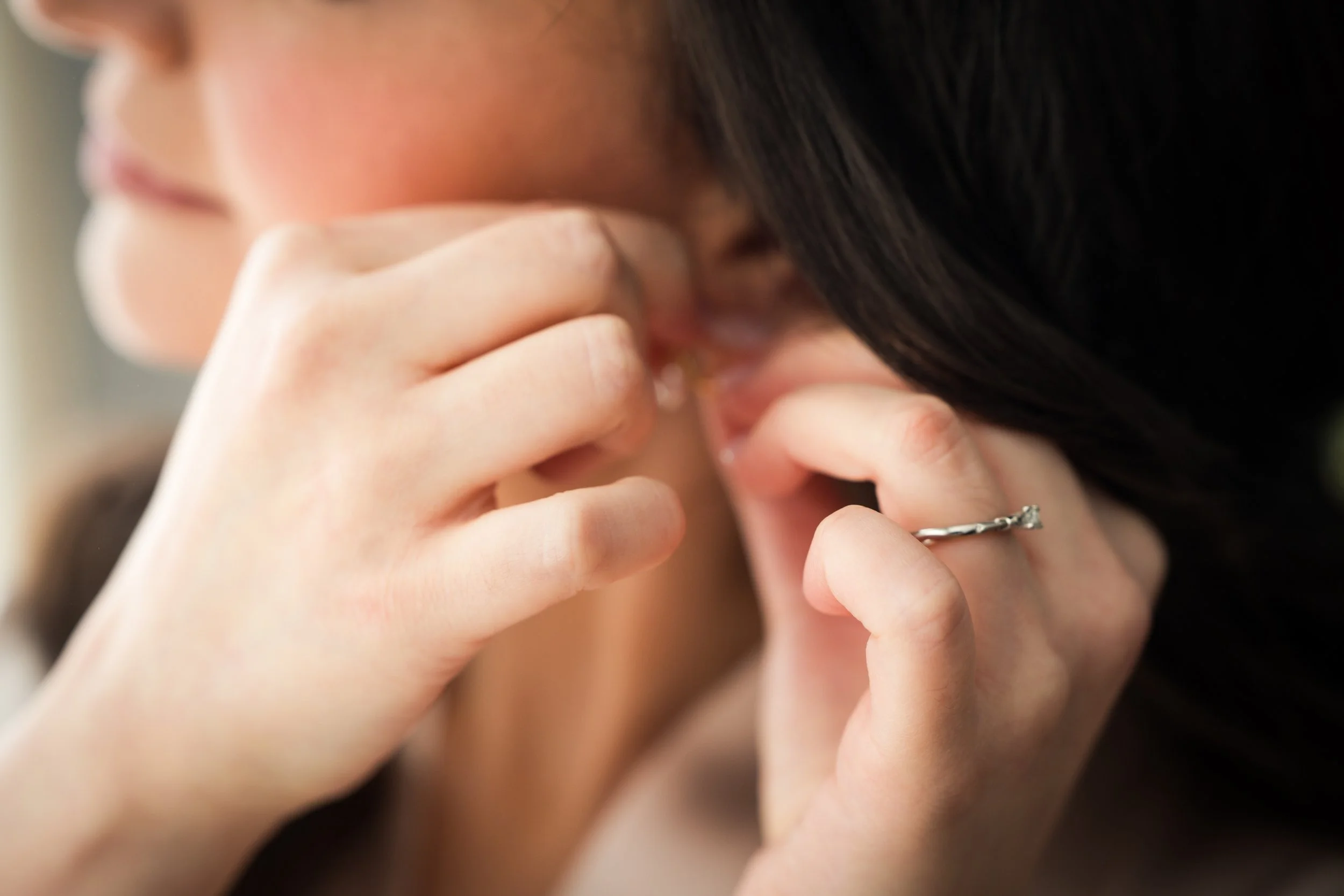 A person putting in an earring with their hands, focused on the earlobe and jewelry.