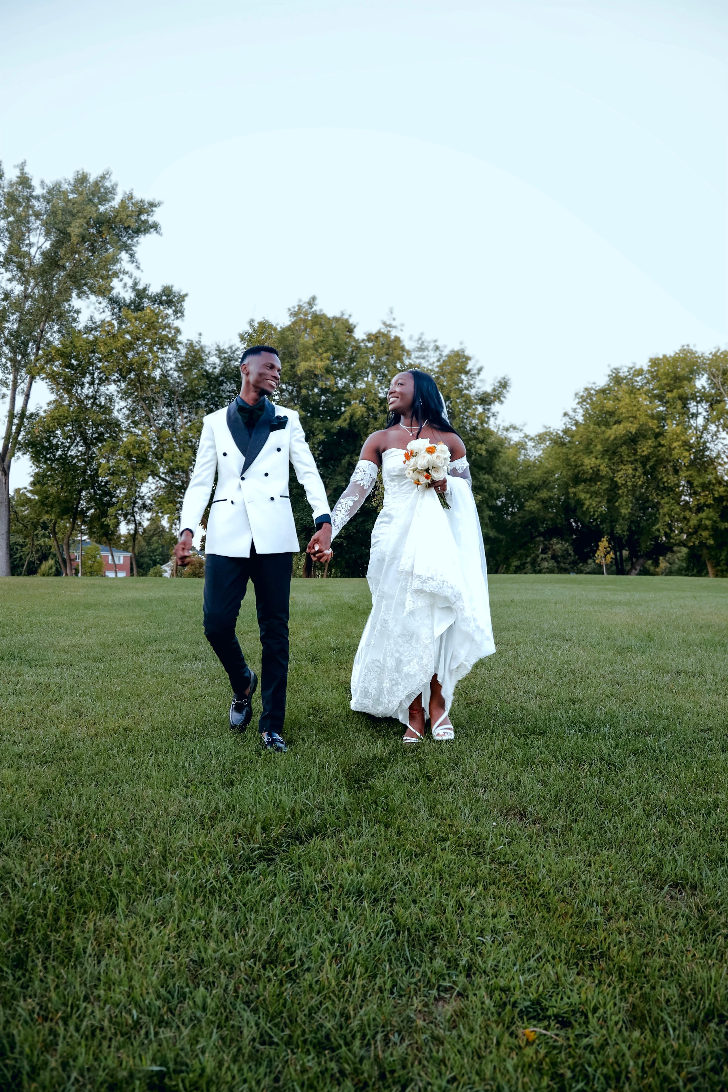 A joyful newlywed couple walking hand in hand across a lush green lawn, dressed in an elegant white gown and tailored suit, symbolizing love and timeless storytelling. Founders of Endless Vows Montreal based luxury wedding photography and videography