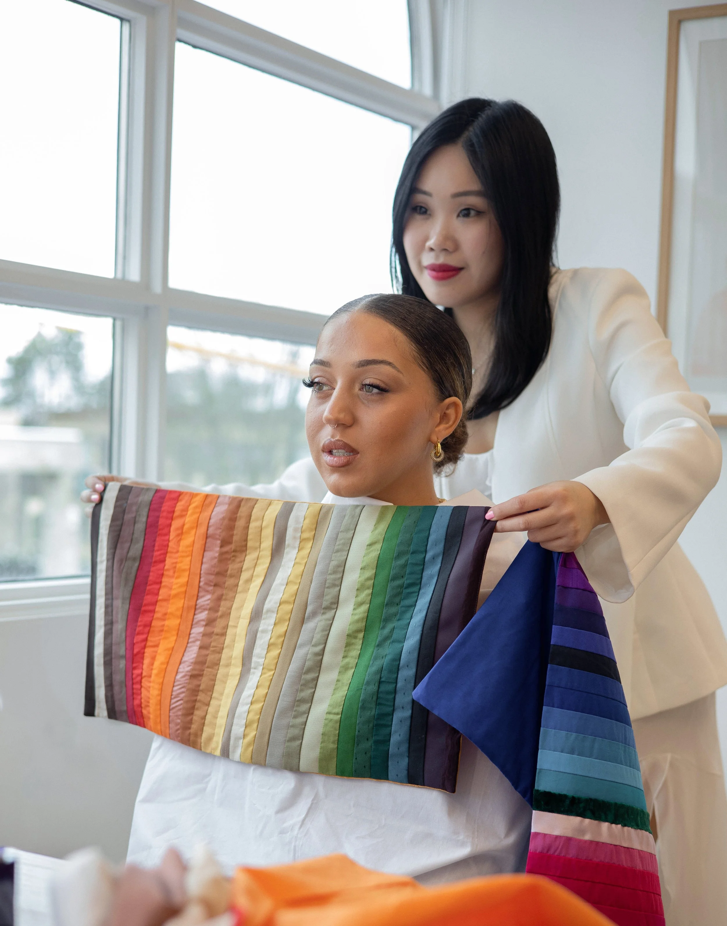 A personal colour analyst drapes a true autumn fabric swatch over a client in a bright studio with large windows, evaluating warm seasonal colour tones in natural daylight.