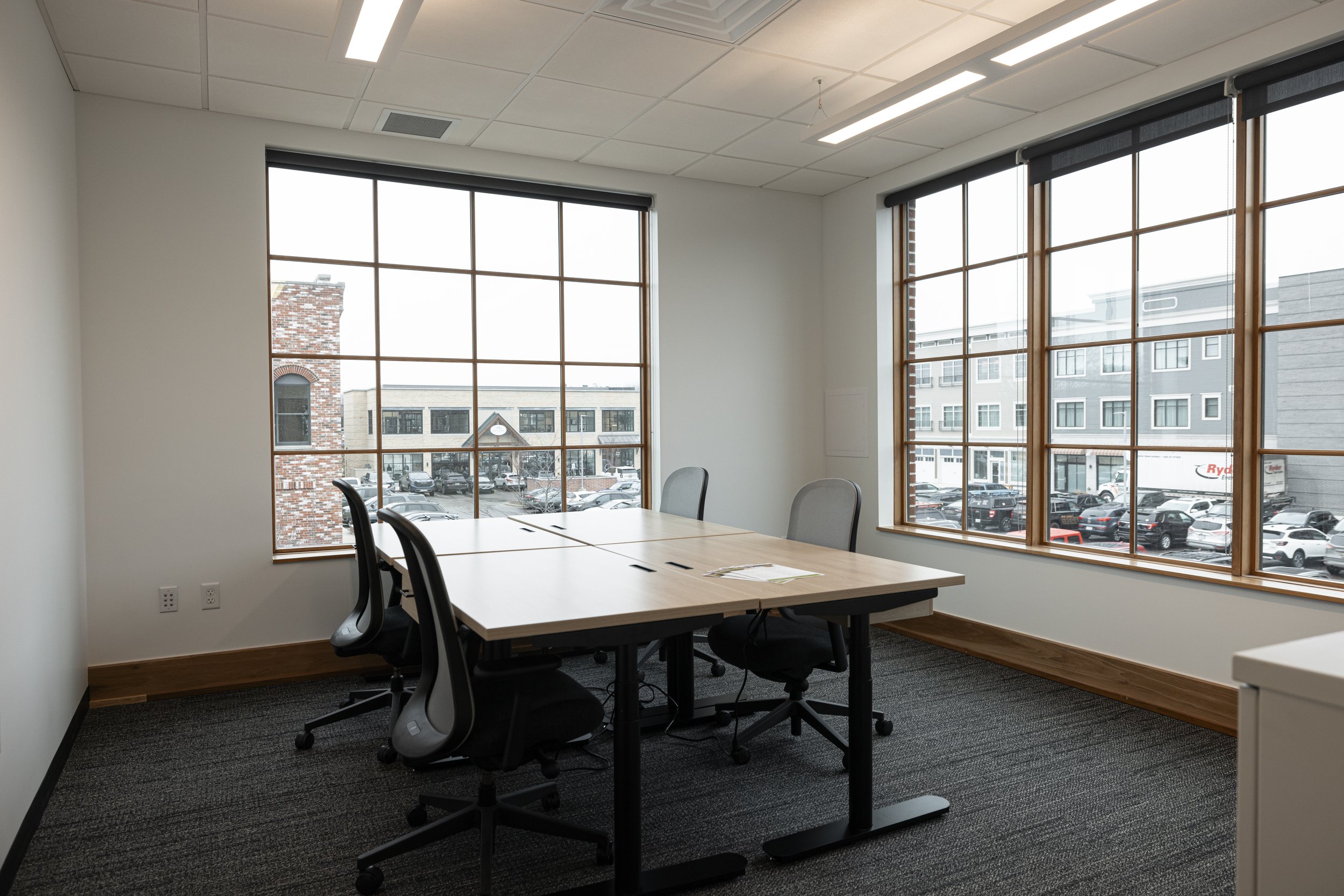 Empty conference room with large windows, white walls, black chairs, and a wooden table.