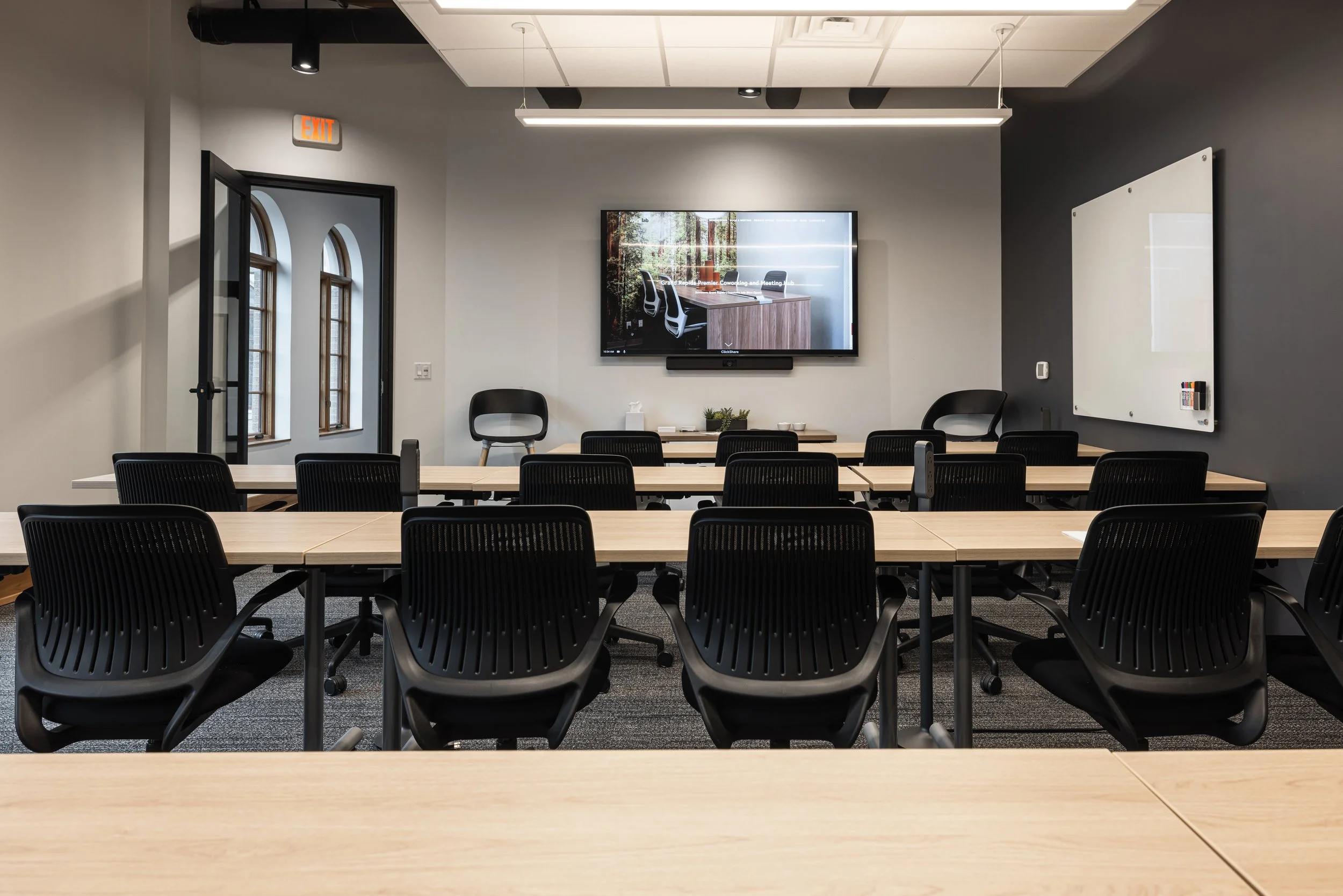A smiling man with glasses and a beard, wearing a tan sweater, sitting at a conference table during a meeting.