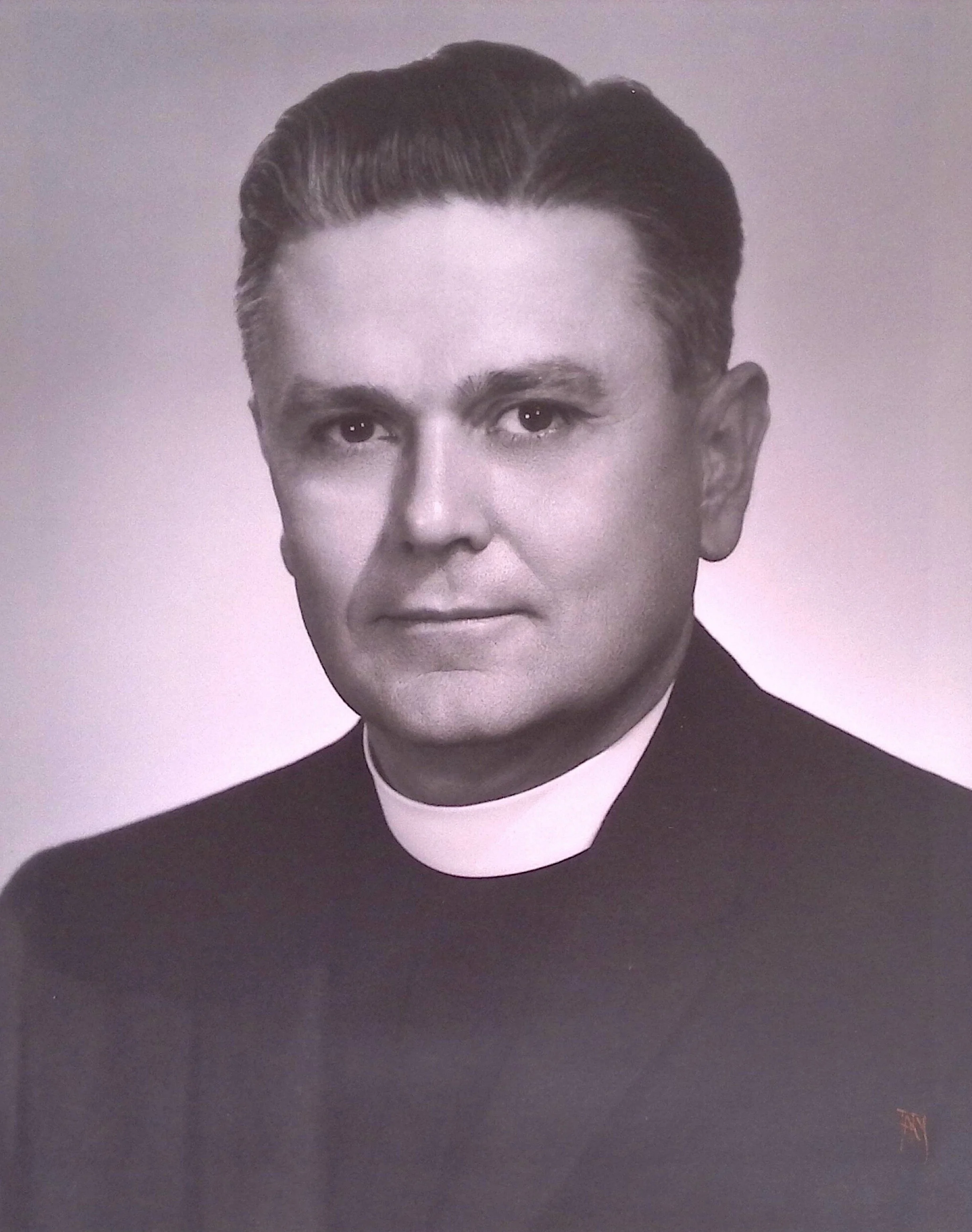 Black and white portrait of a man with combed-back hair, wearing a clerical collar and suit, looking directly at the camera.
