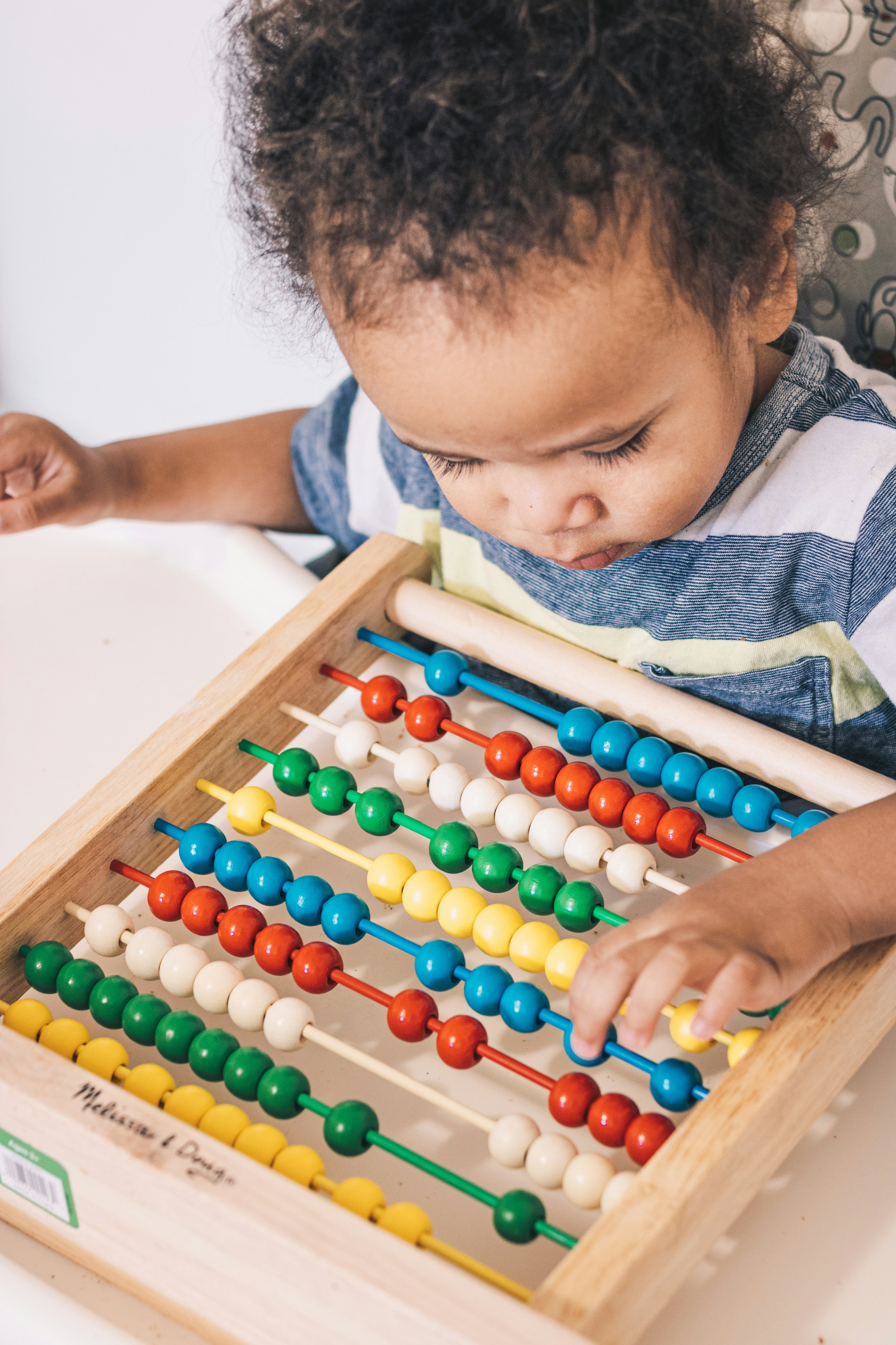 A young child with curly hair playing with a colorful wooden abacus with multiple rows of beads in red, white, green, yellow, and blue.