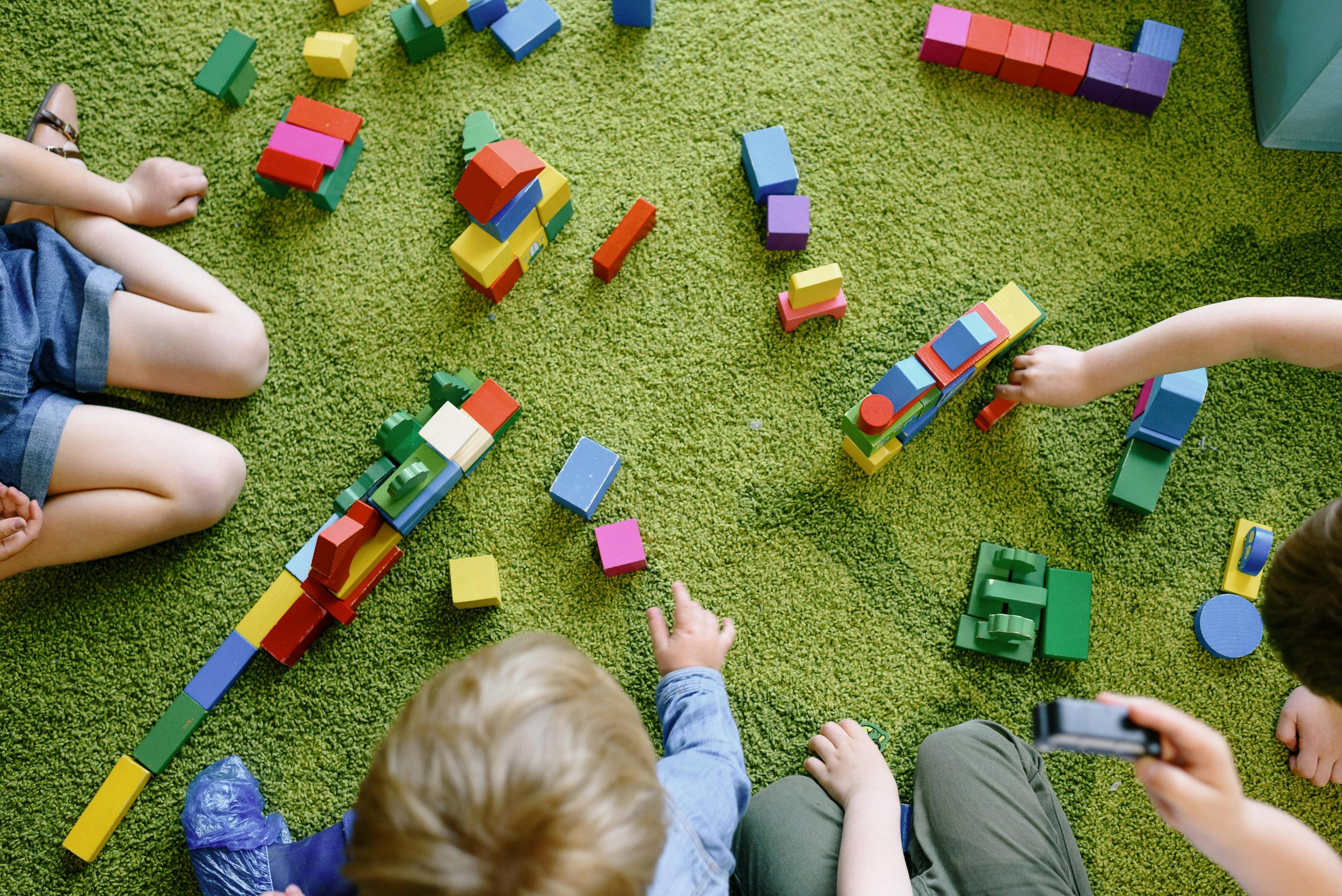 Children playing with colorful building blocks on a green carpet.