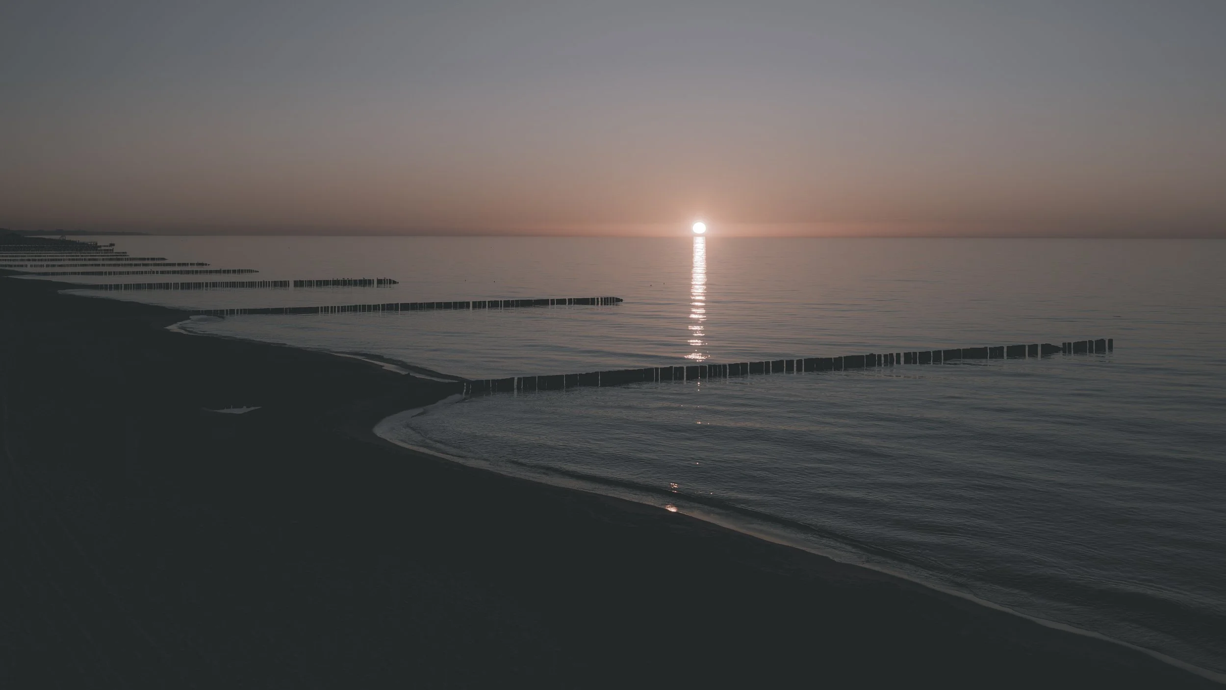 Letztes Licht
Die tief stehende Sonne und ihre Spiegelung setzen einen hellen Akzent zwischen ruhigem Wasser, Strand und den Linien der Buhnen.
