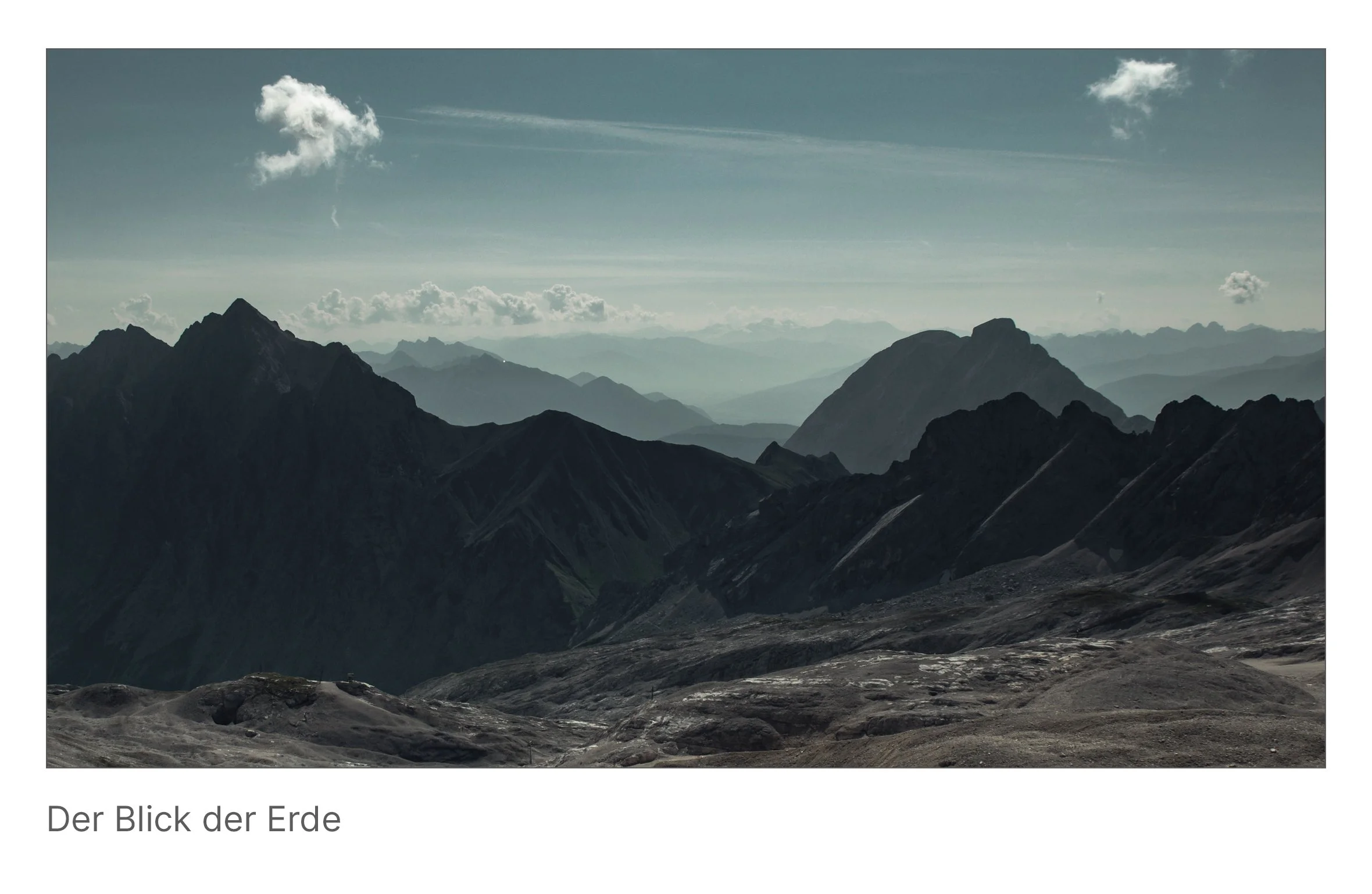Weitläufige Alpenlandschaft von der Zugspitze aus gesehen, mit rauen Bergkämmen unter einem blassen Himmel – symbolisch für die stille Kraft der Natur.