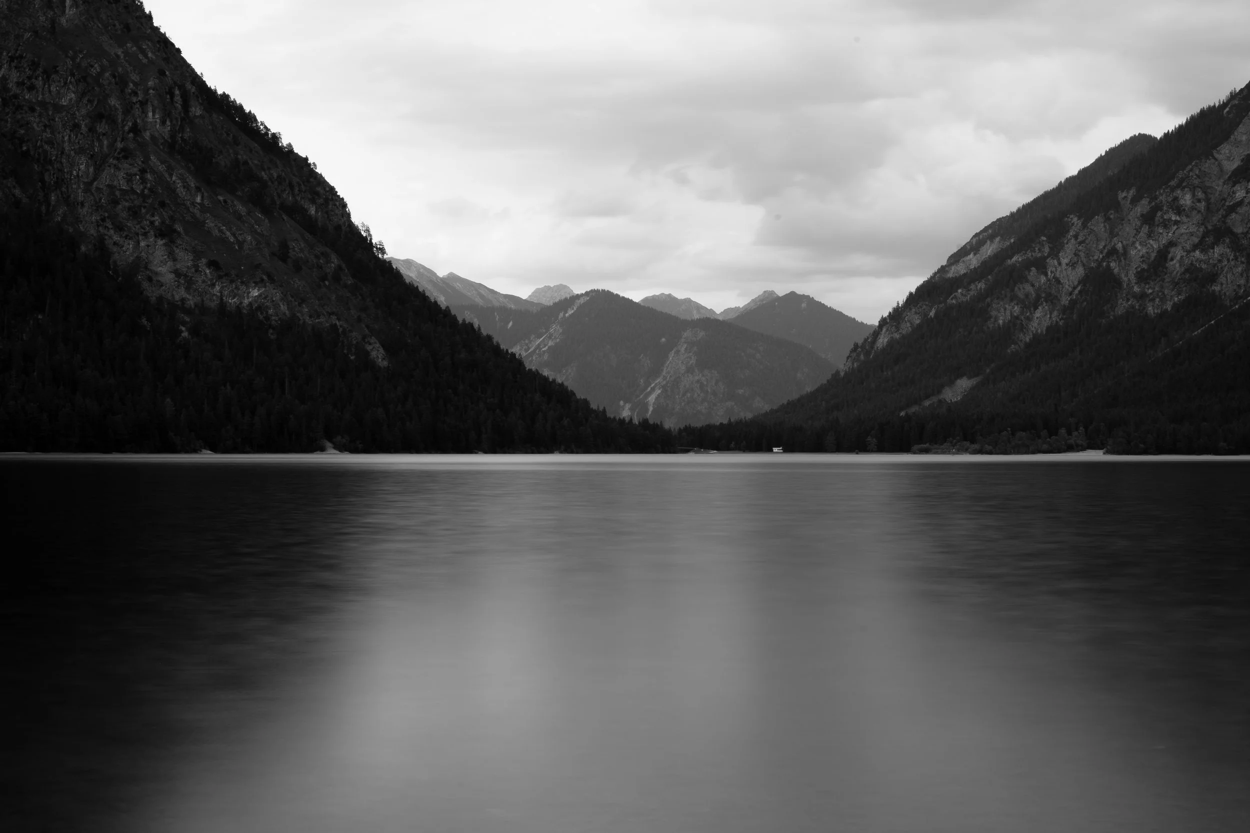 Bergsee zwischen Gebirgshängen
Langzeitbelichtung eines Bergsees zwischen dunklen Gebirgshängen unter bewölktem Himmel – Fine Art Nature Photography von ReBlick.
